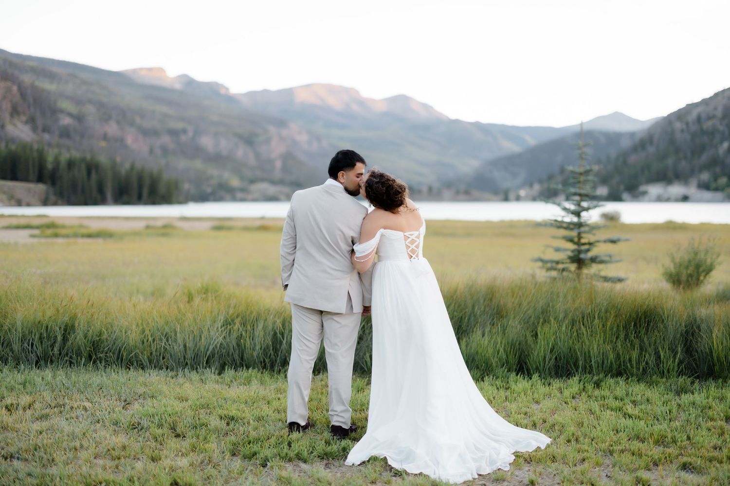 Bride and groom embrace facing mountain lake backdrop in Colorado outdoor wedding ceremony.