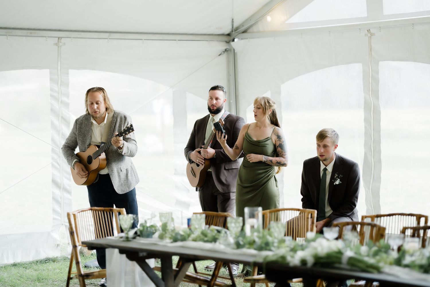 Musicians performing at an elegant outdoor wedding reception under a white tent with greenery table decor.