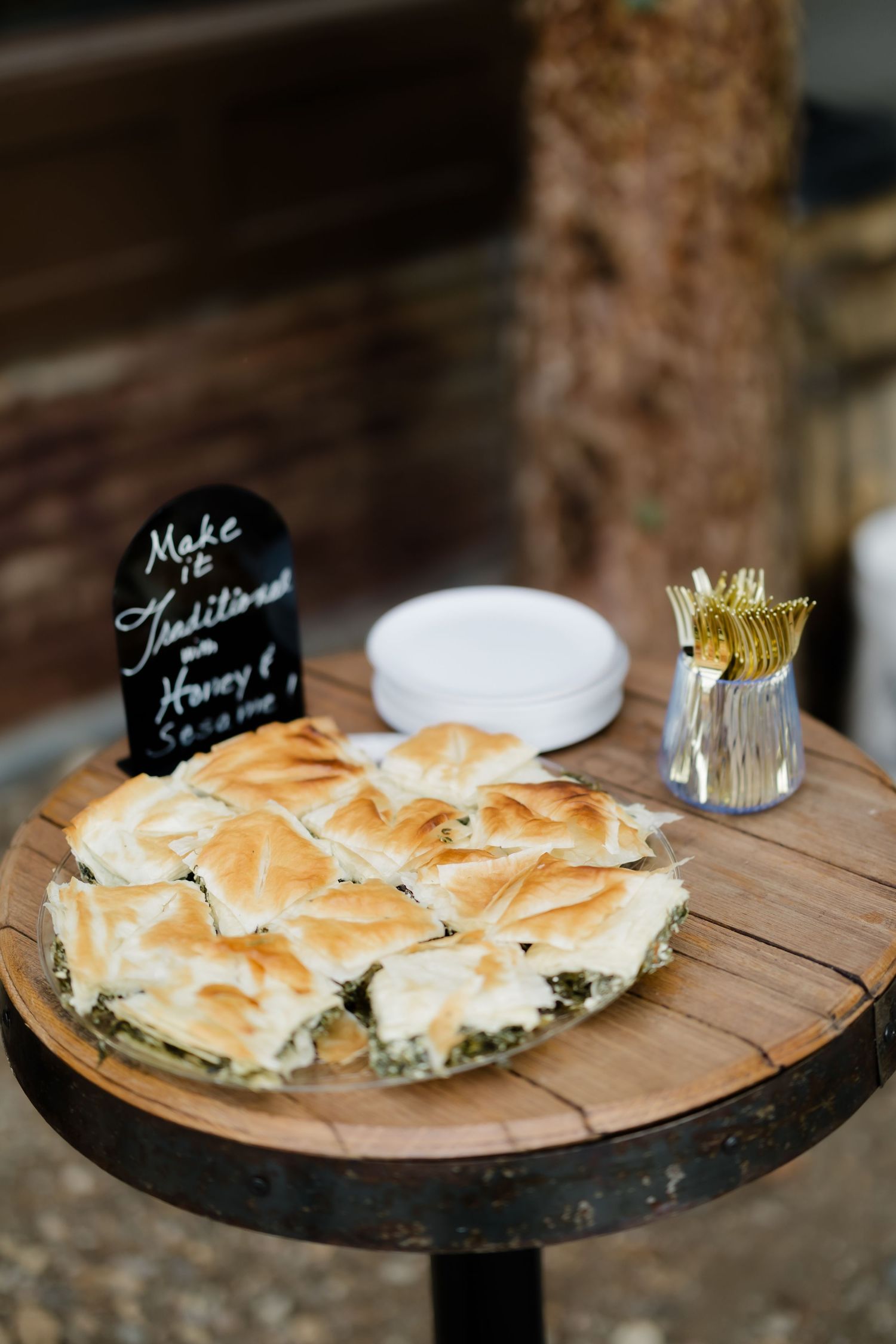 Spinach and feta phyllo pie sliced on a wooden board with gold forks and plates at a catered event.