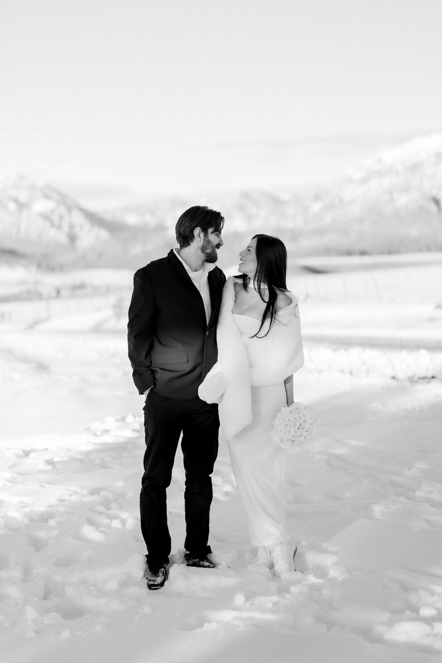 Black and white portrait of bride and groom gazing at each other with snowy mountain valley in the background.