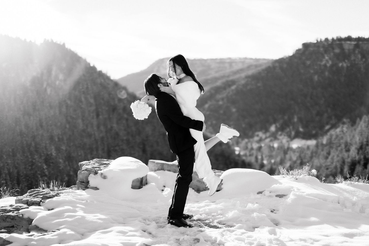 Groom lifting bride in black and white photo on snowy mountain wedding day.