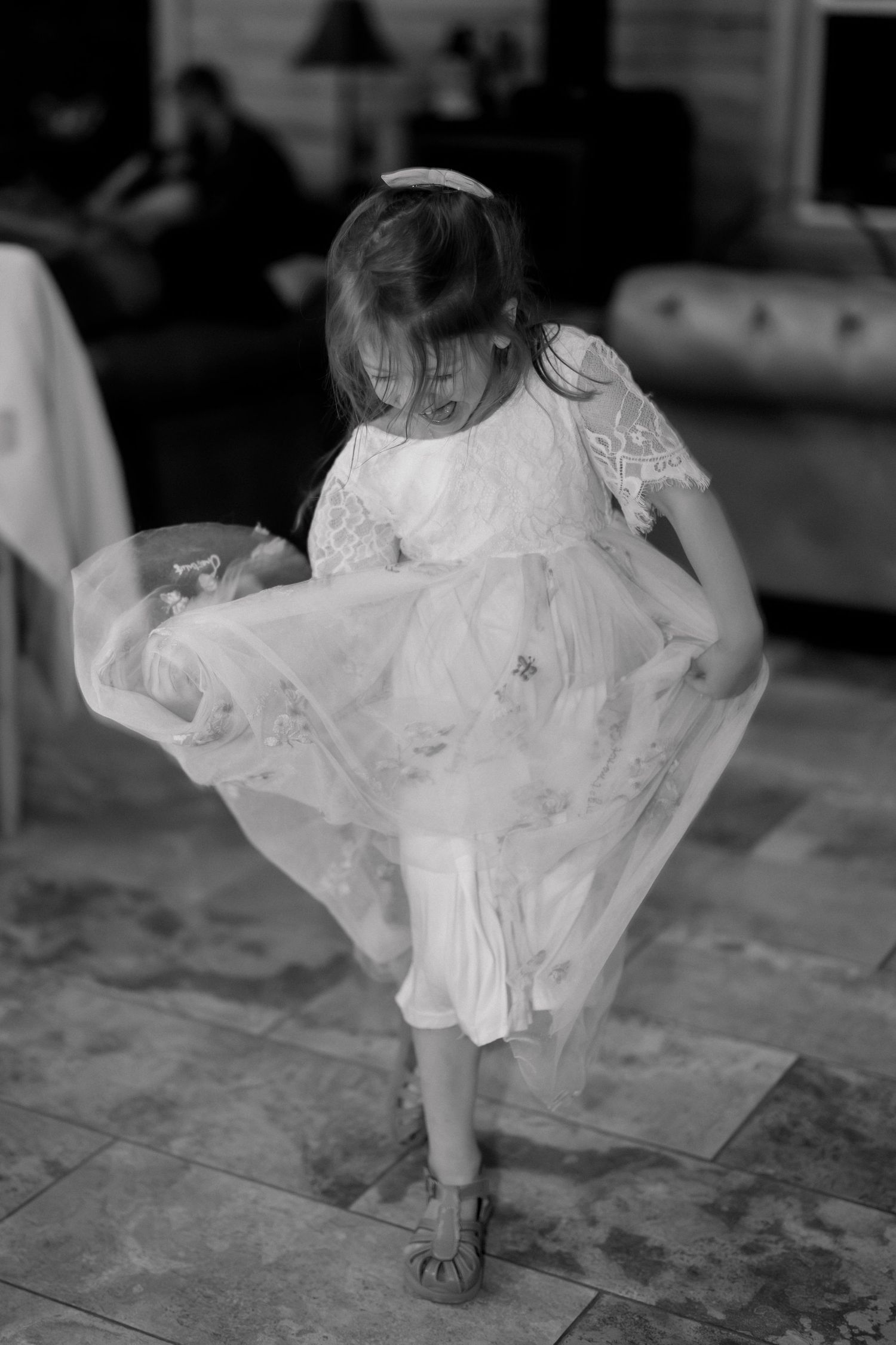Black and white photo of a young girl in a white dress twirling indoors.