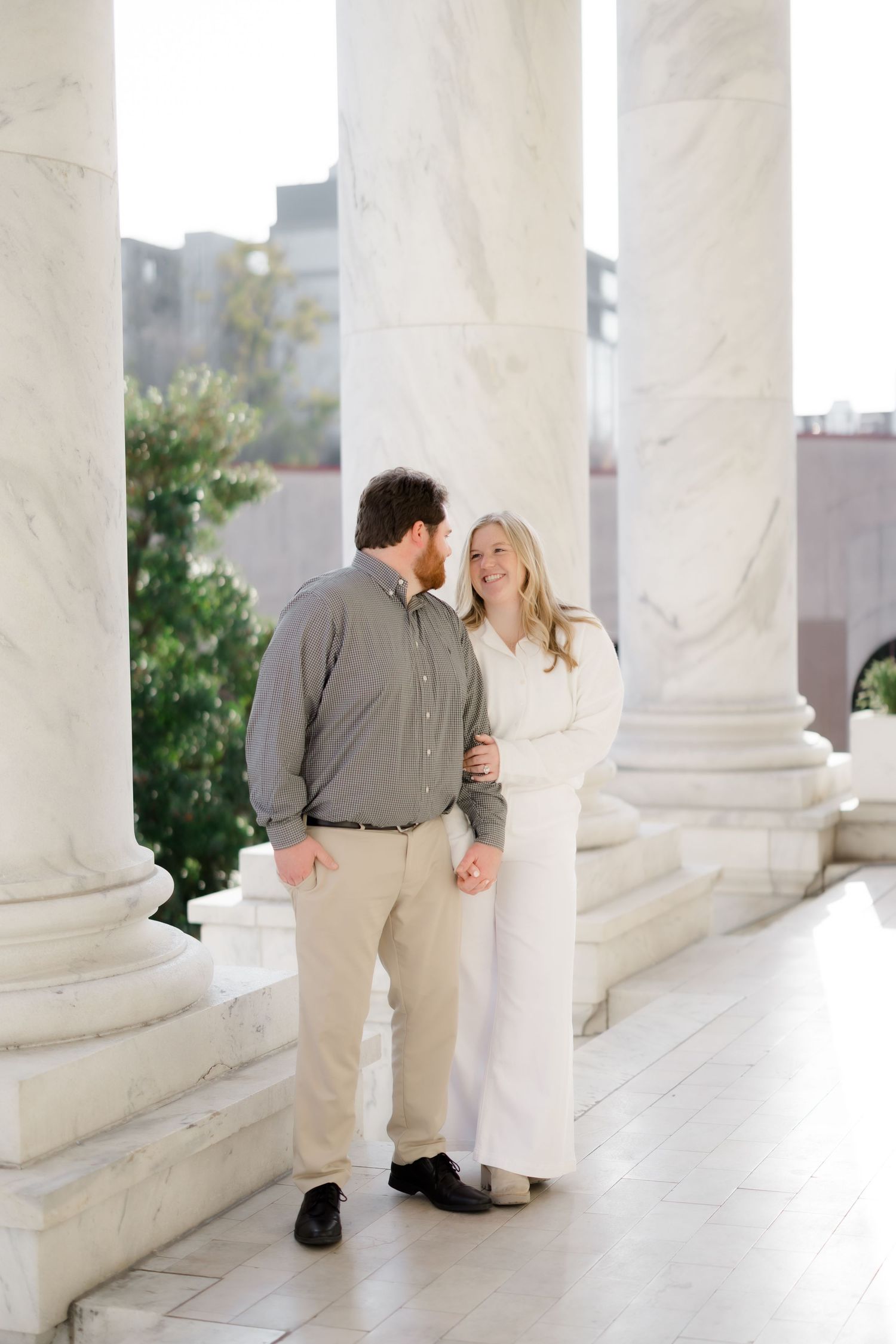 Couple smiling at each other between marble columns at an elegant building during their engagement session.