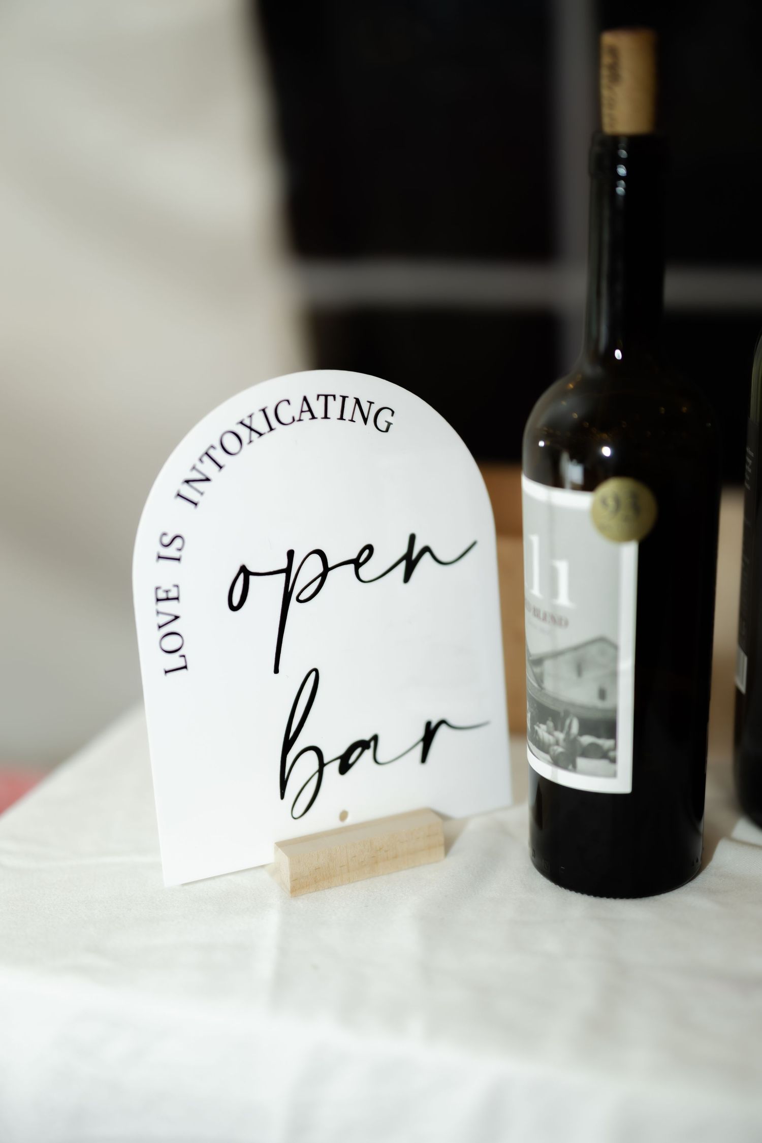Elegant open bar sign with cursive text and love is intoxicating quote beside a dark wine bottle.