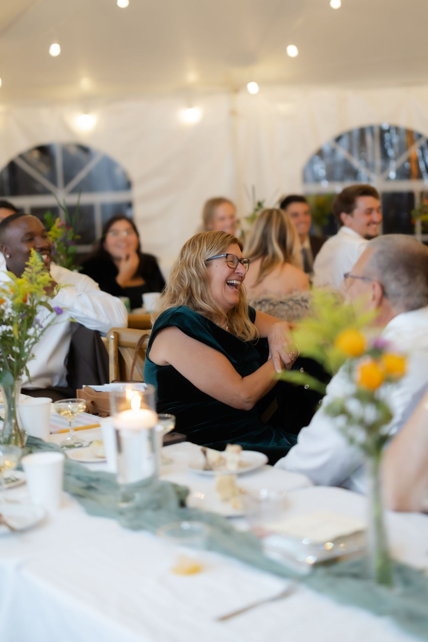 Guests laughing and celebrating at an elegant wedding reception under a white tent with string lights.