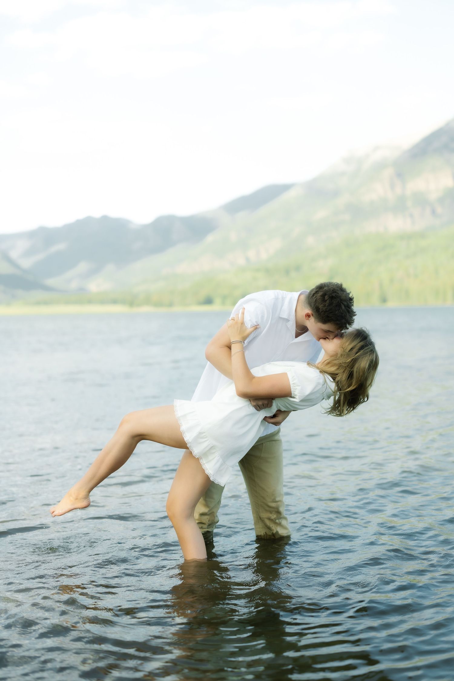 Romantic couple in white clothing creating playful poses in a mountain lake.