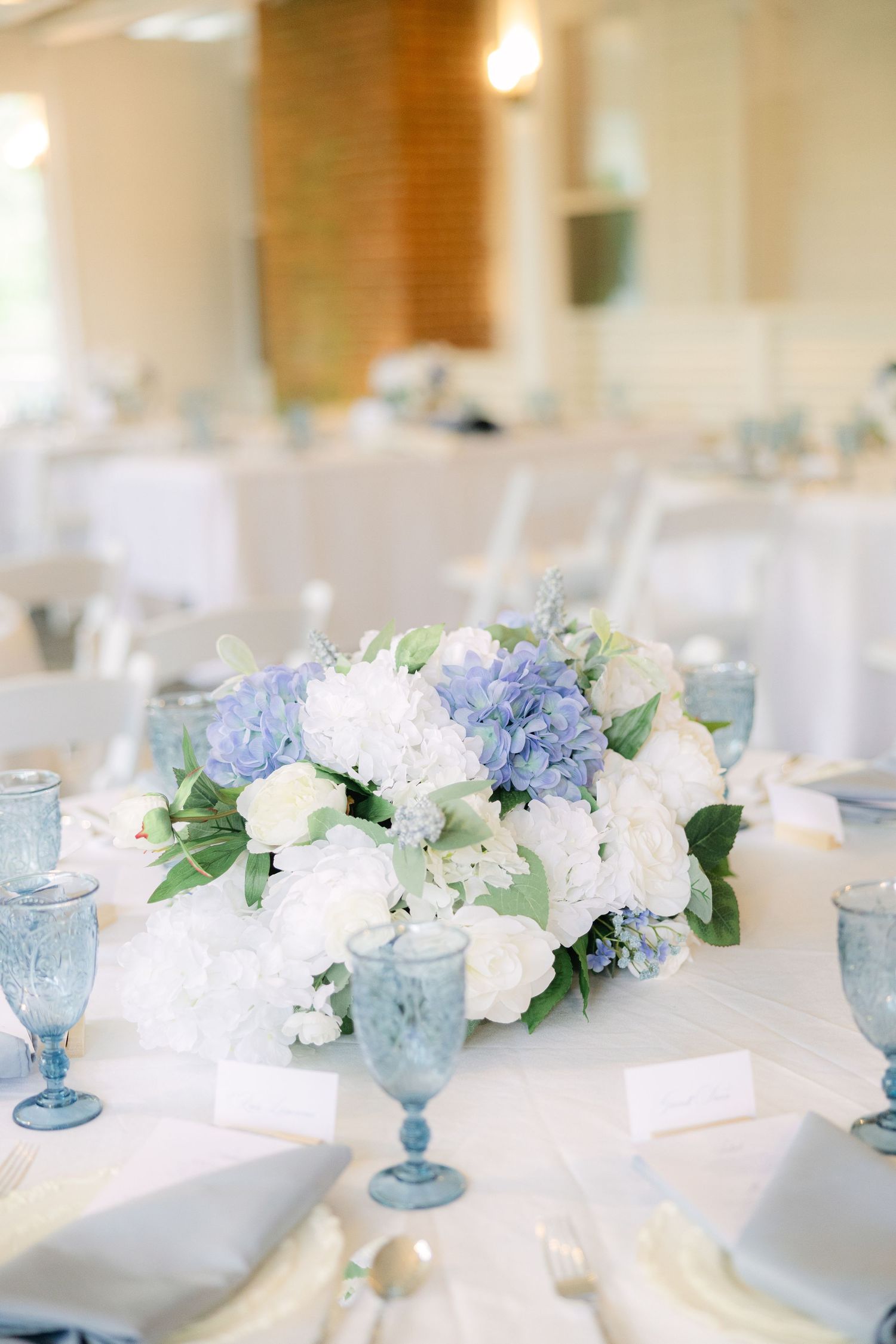 Elegant wedding reception table with blue and white floral centerpieces and vintage blue glassware in soft lighting.