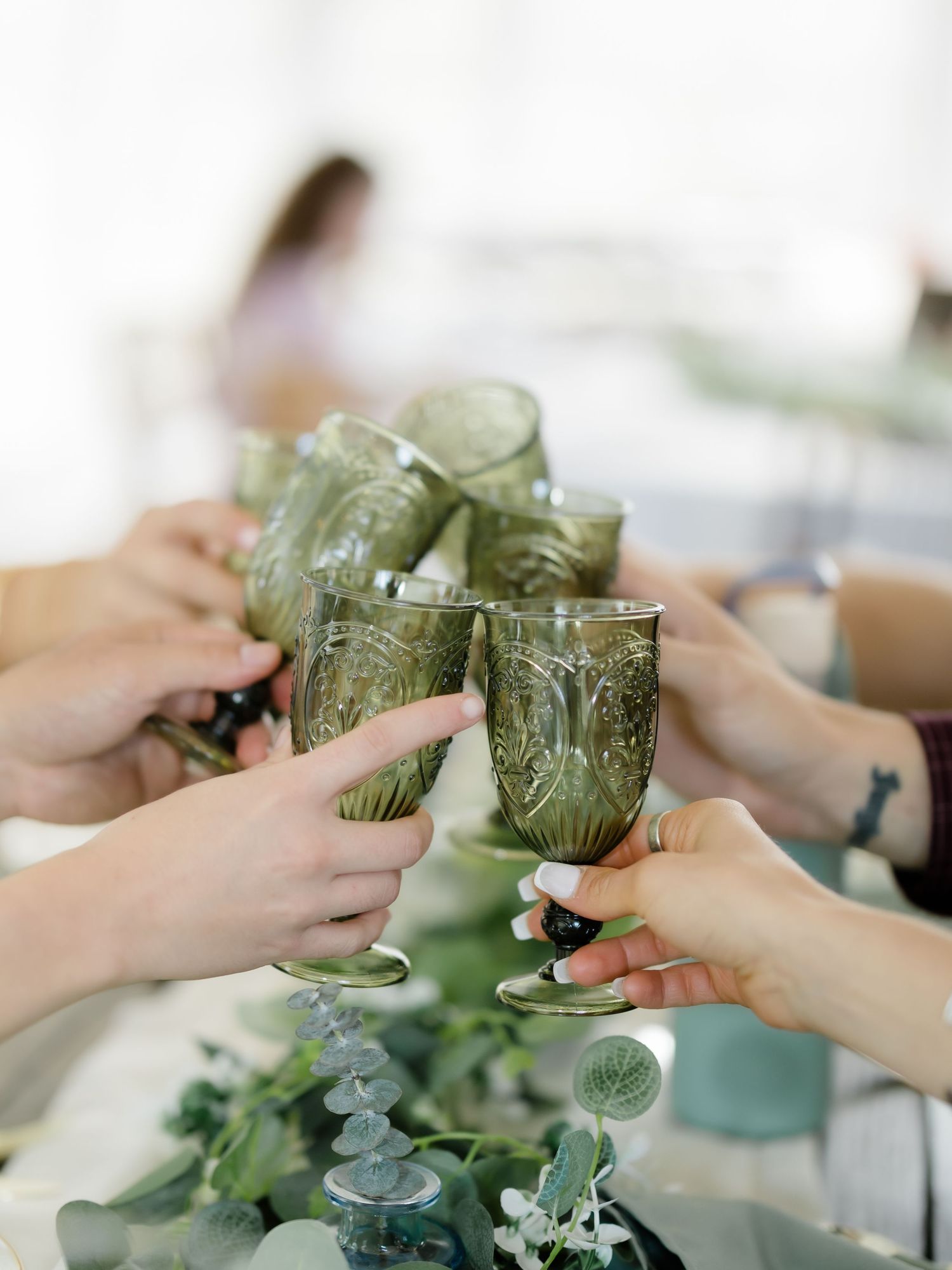 People toasting with ornate green goblets at an elegant wedding reception table adorned with eucalyptus greenery.