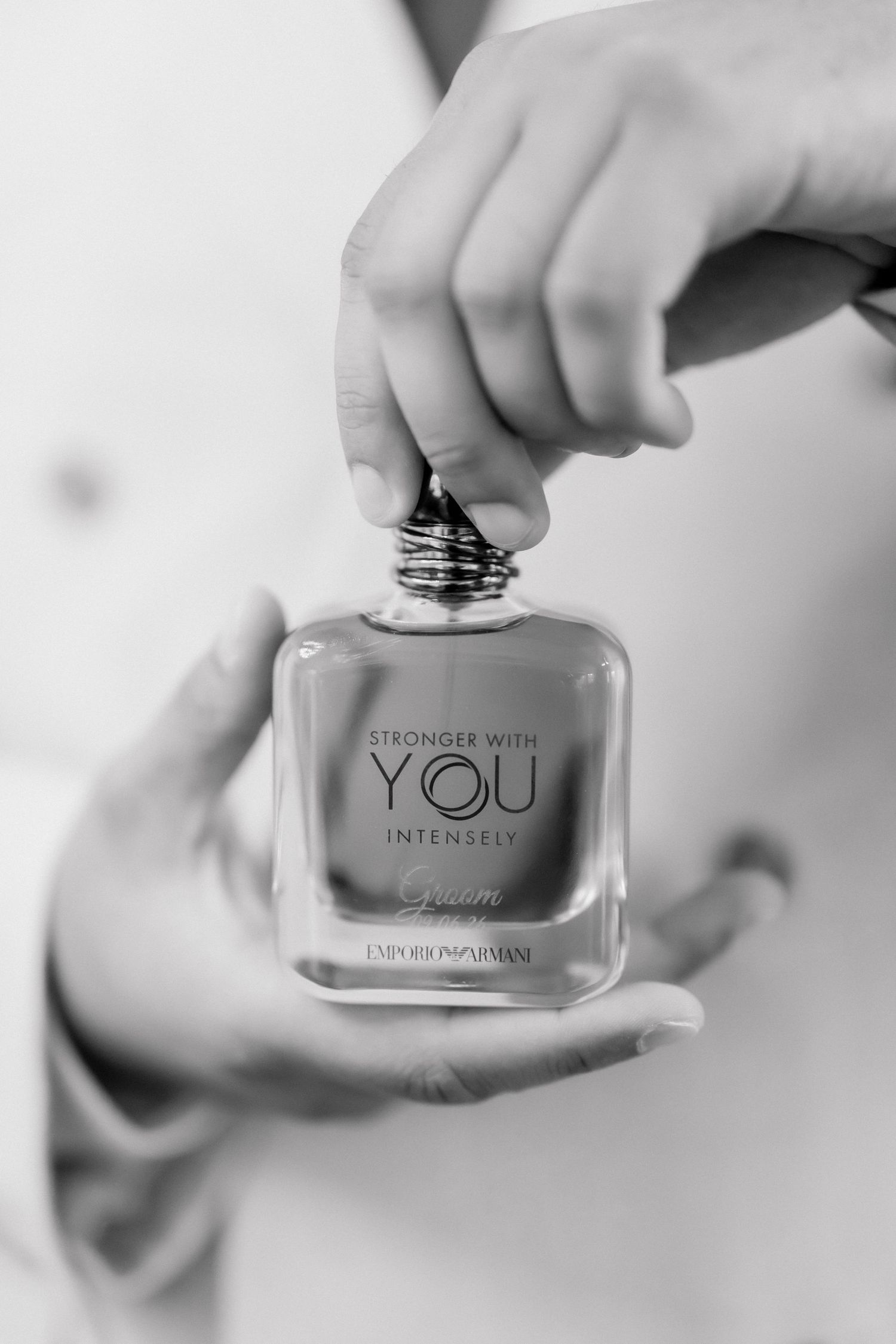 Hands holding Emporio Armani Stronger With You Intensely perfume bottle in black and white photo.