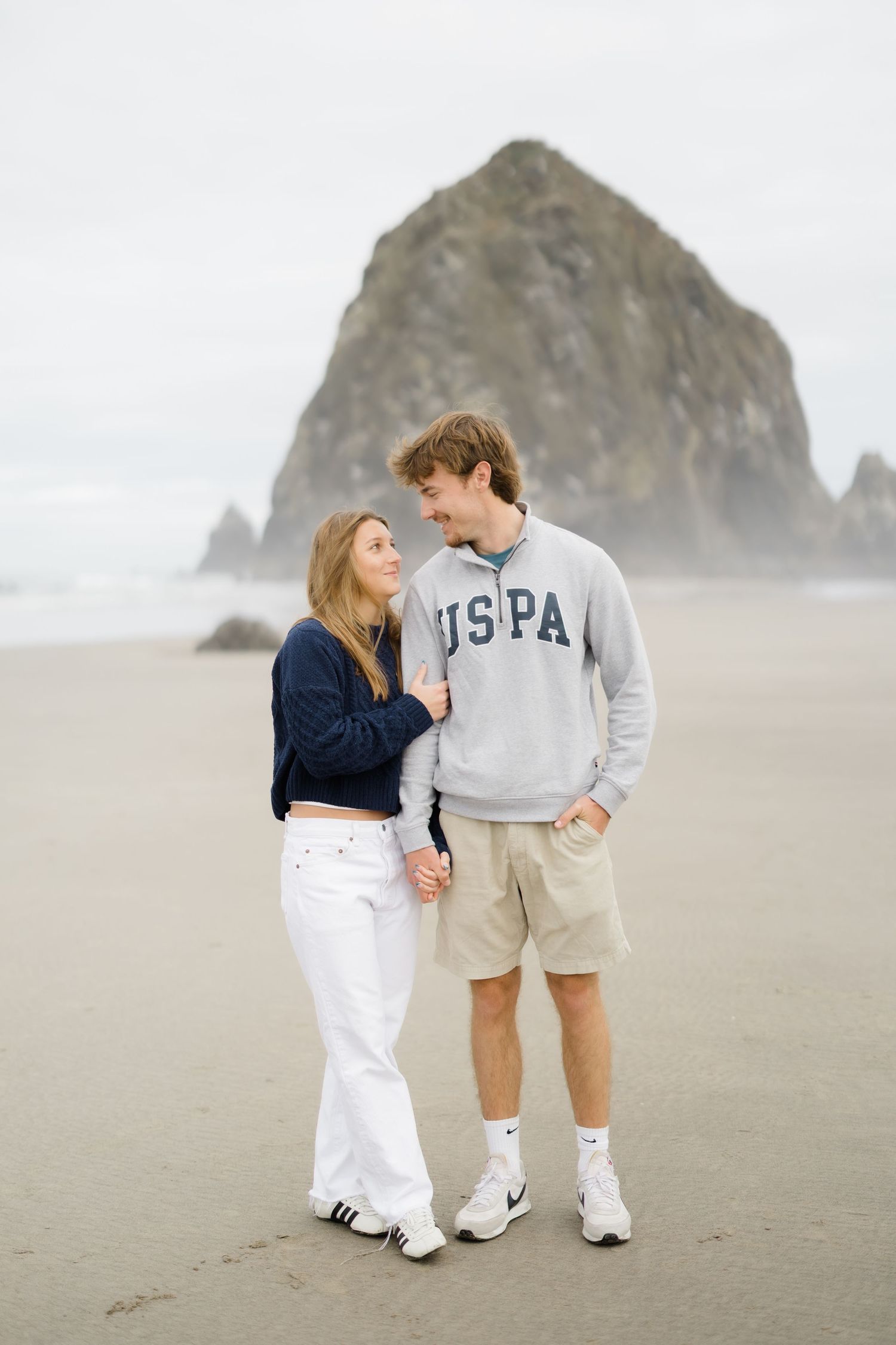 Couple holding hands on a sandy beach with Haystack Rock in the background at Cannon Beach, Oregon.
