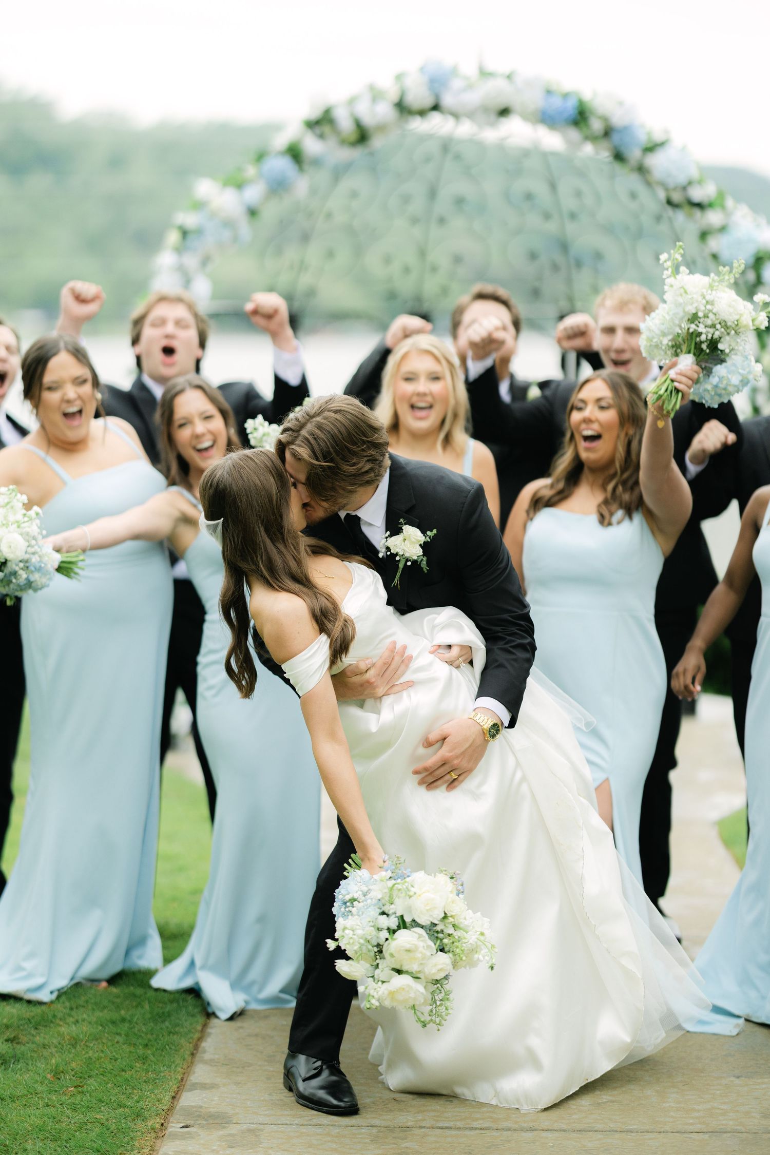 Bride and groom dip and kiss portrait with wedding party cheering