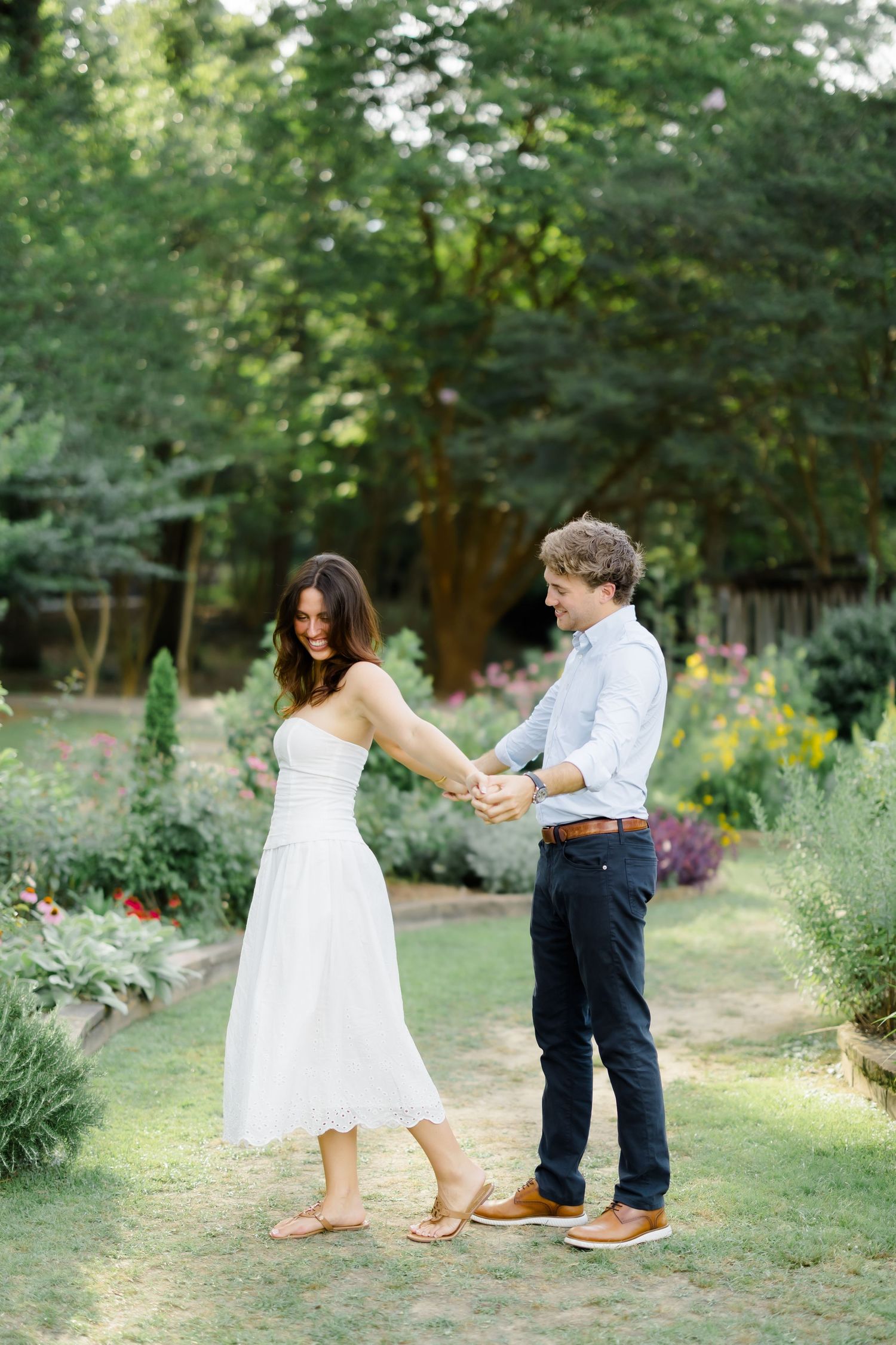 Couple dancing together in a lush garden, woman in white dress, man in blue shirt and navy pants.