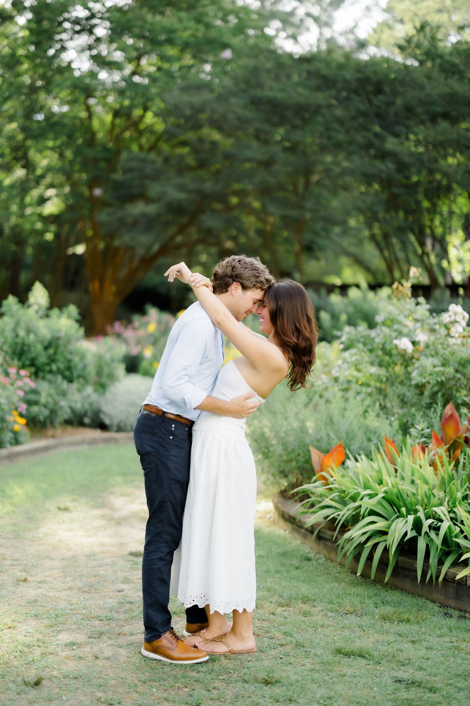 A couple shares a romantic dance in a lush garden, the woman in a white dress, the man in navy pants and blue shirt.