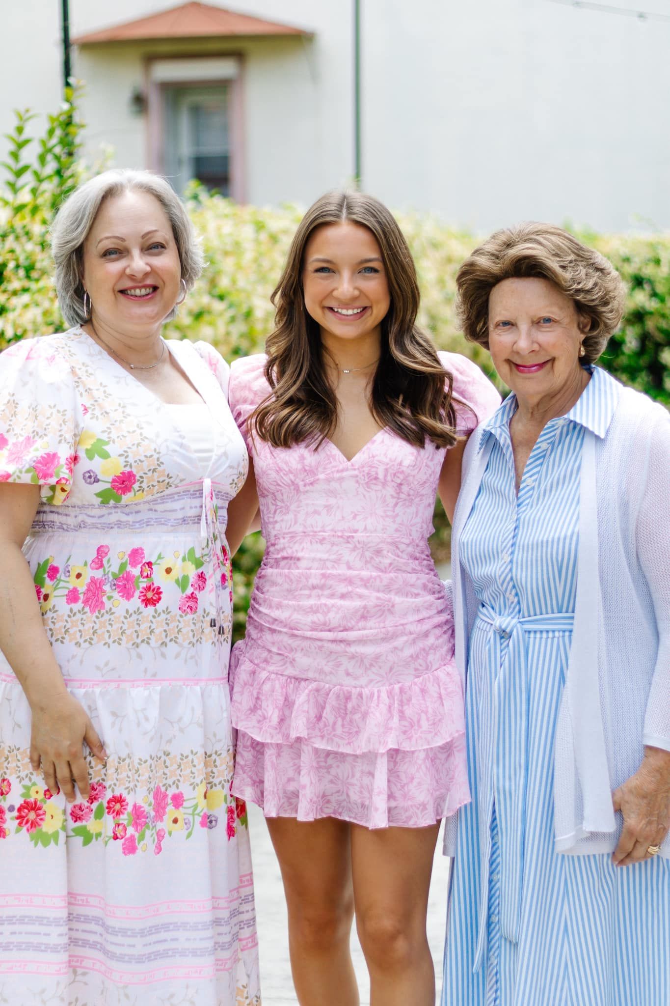 Three generations pose together outdoors wearing coordinating pink and blue dresses in front of a garden in Troy, Alabama.