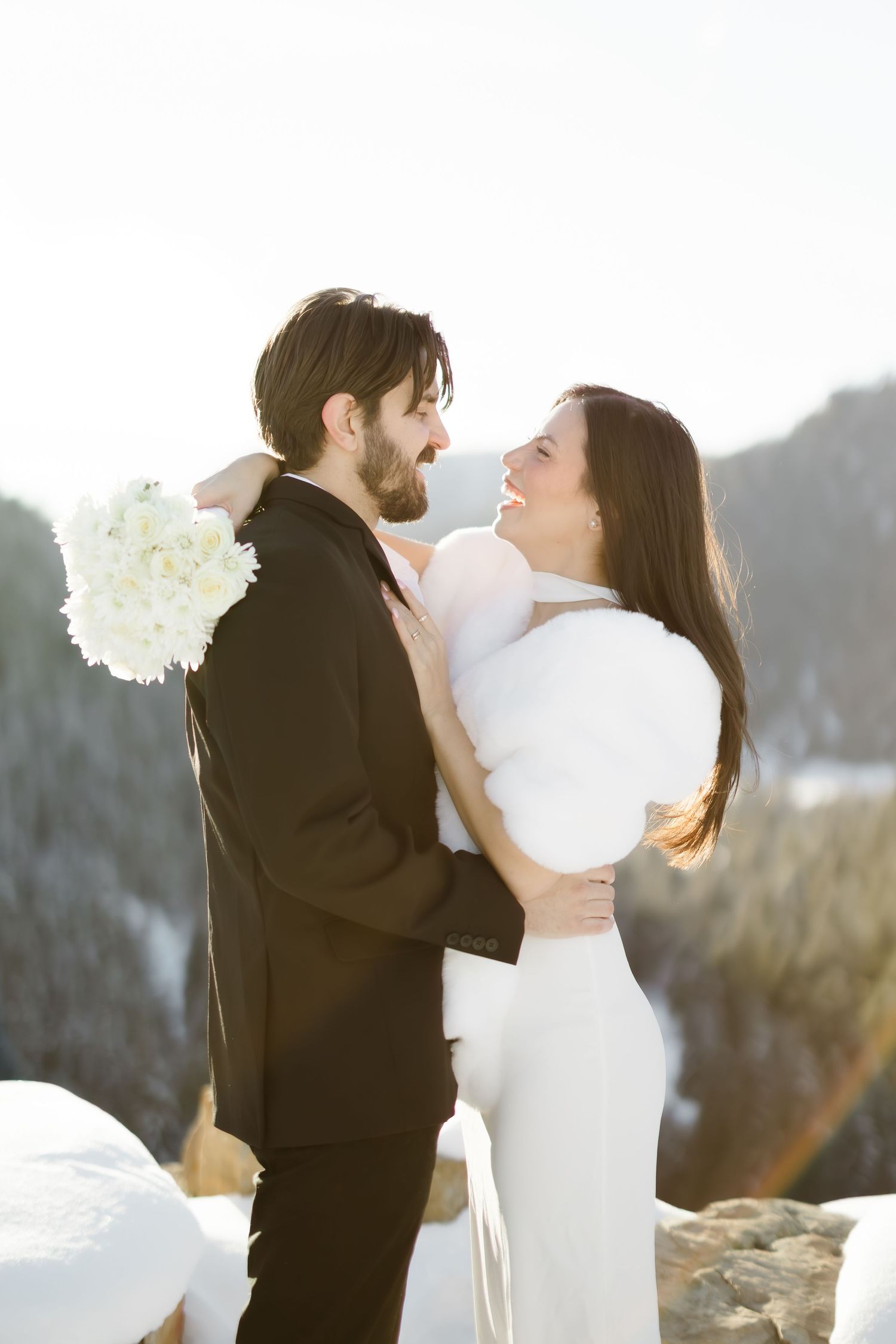Bride and groom embrace and smile at each other during a winter wedding in snowy mountains.