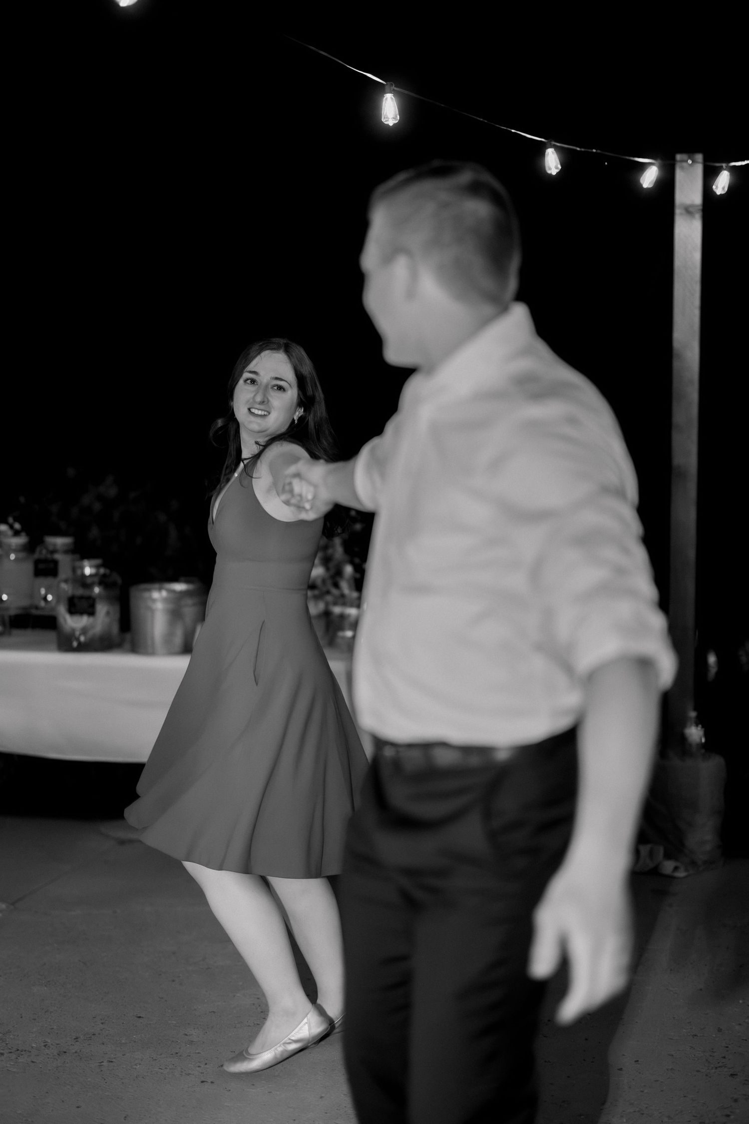 Black and white photo of a smiling woman in a dress dancing with a man at an outdoor evening event.