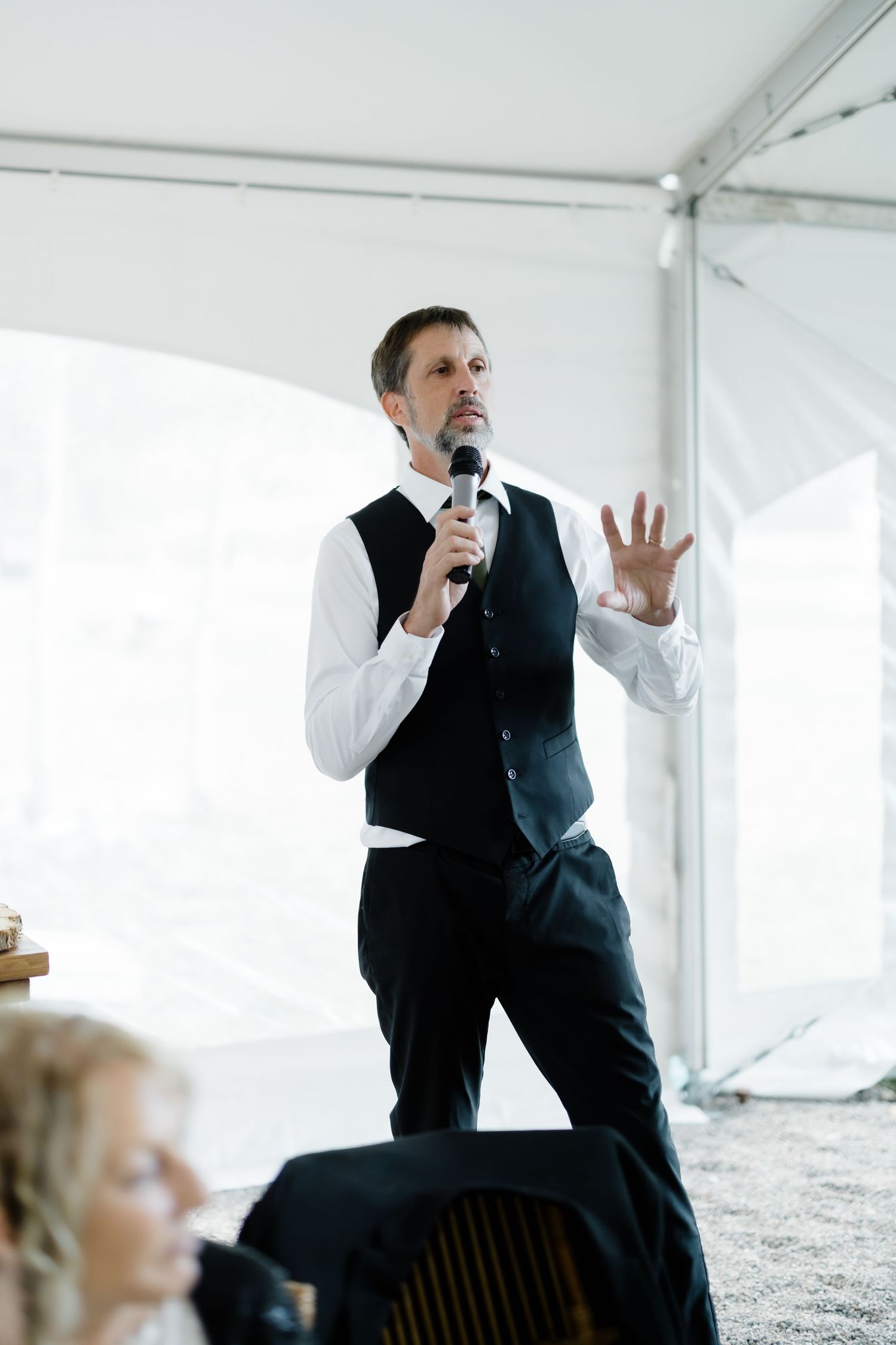 Elegant man in black vest delivers a heartfelt wedding speech with microphone at reception.