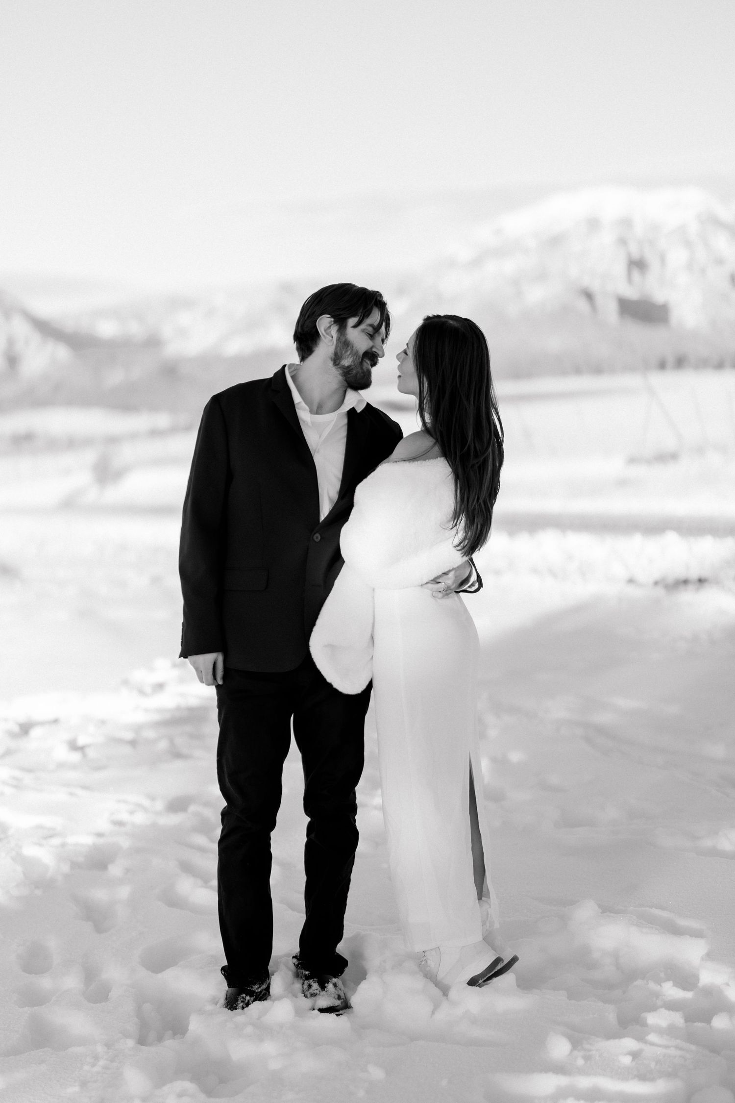 Black and white photo of bride and groom gazing at each other in a snowy mountain setting.