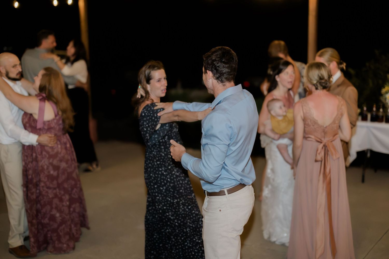 Couples dancing together at an outdoor wedding reception at night, wearing elegant formal attire.