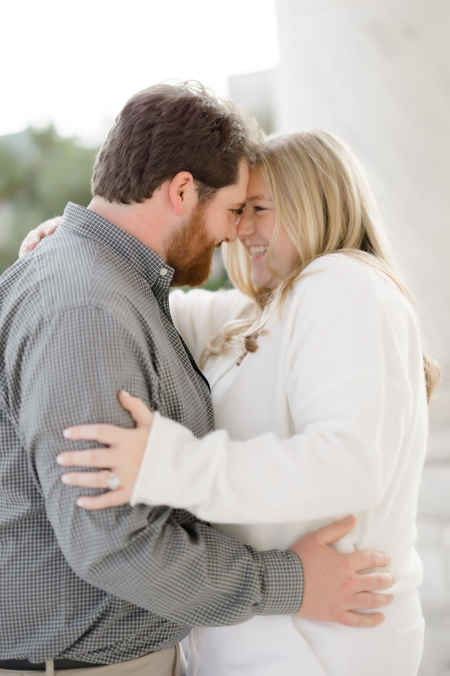 Couple embracing and touching foreheads, laughing together during outdoor engagement photo session.