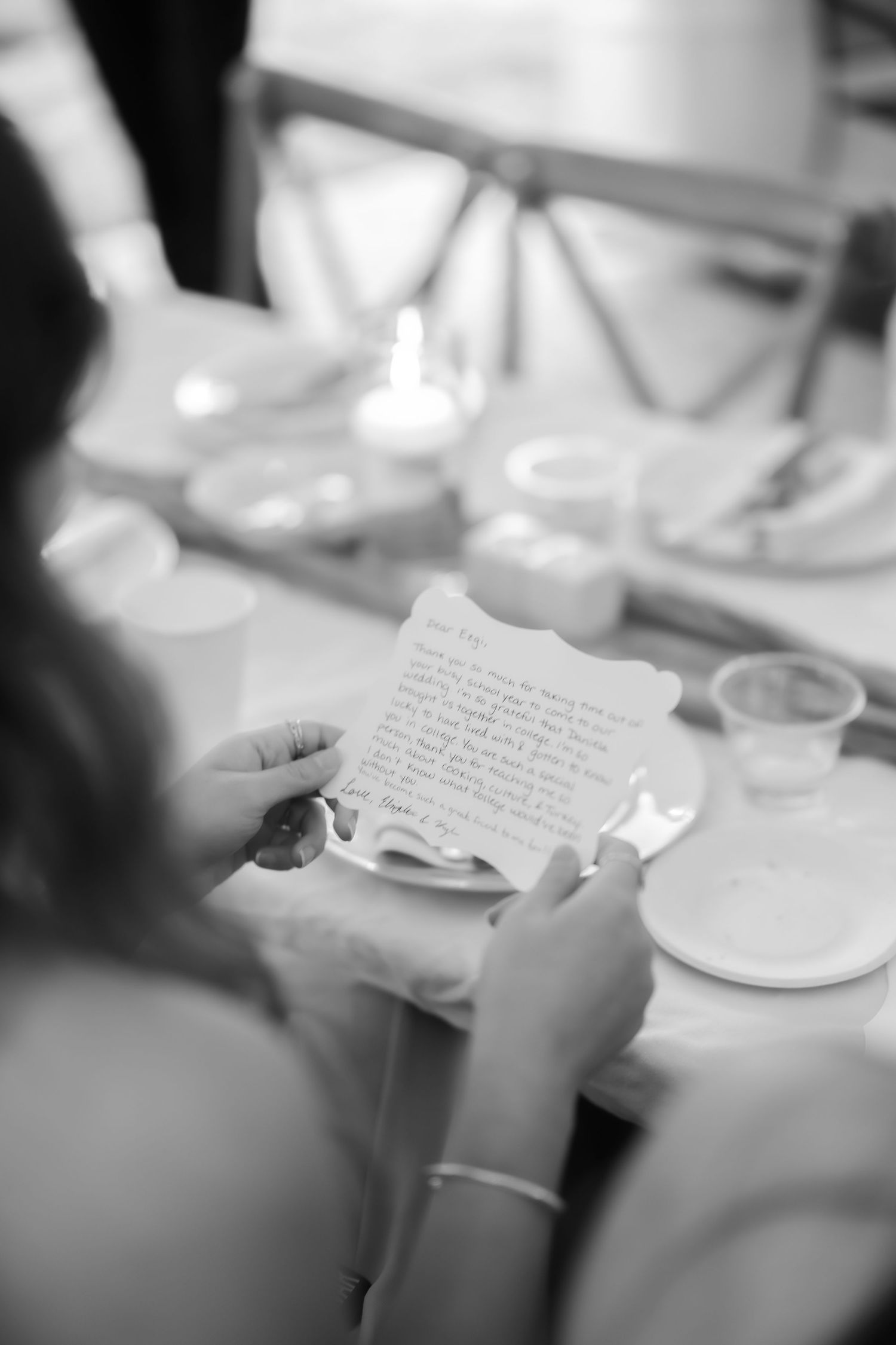 Black and white photo of a bride reading a handwritten letter at a wedding reception dinner table.