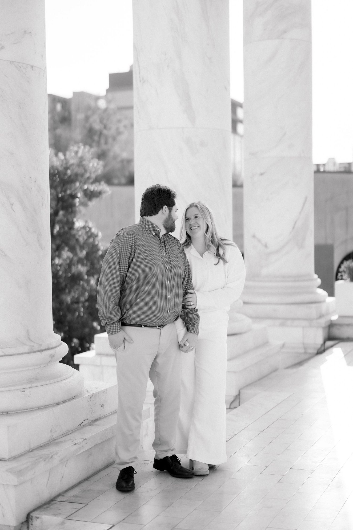 Couple sharing a romantic moment between marble columns in black and white photo.