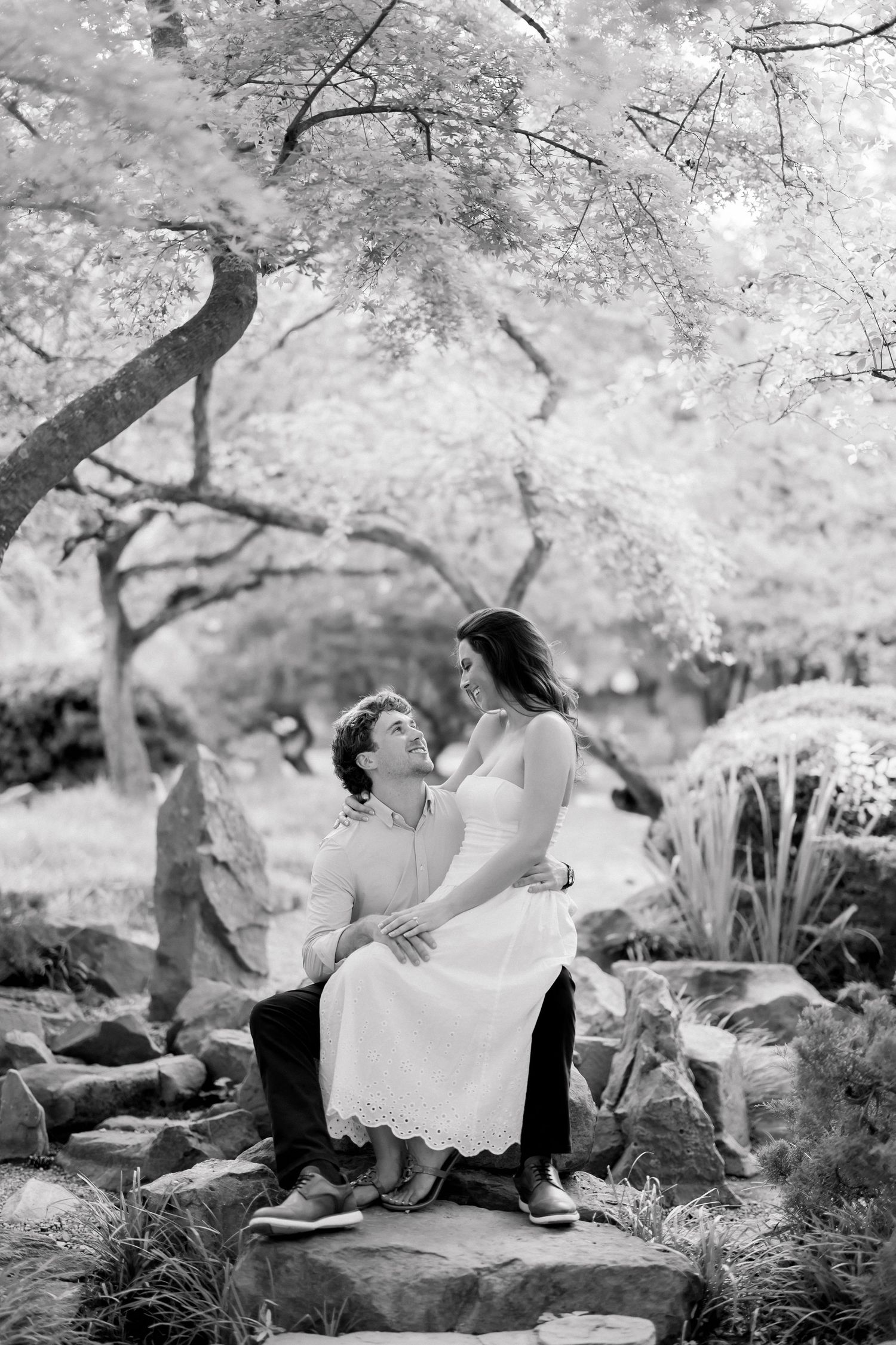 Black and white photo of couple sitting on stone steps under blooming trees in a serene garden.