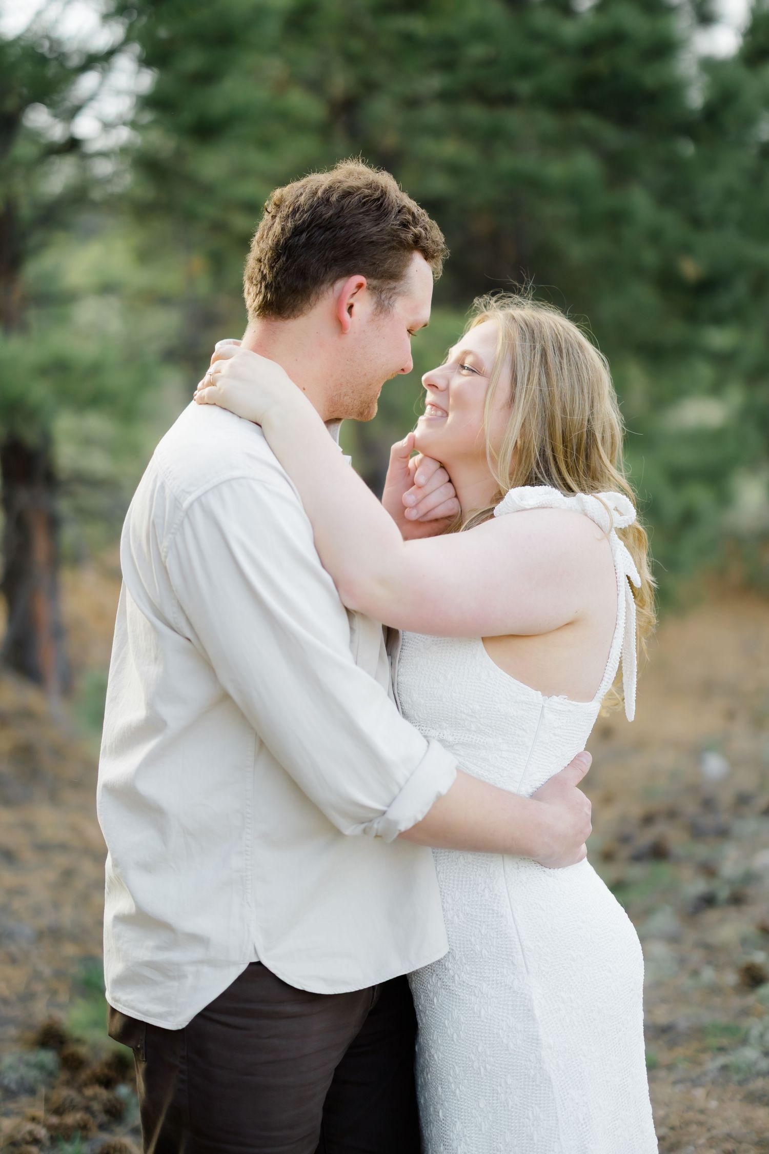 Laughing couple embracing warmly in a forest setting during a golden hour engagement photo session.