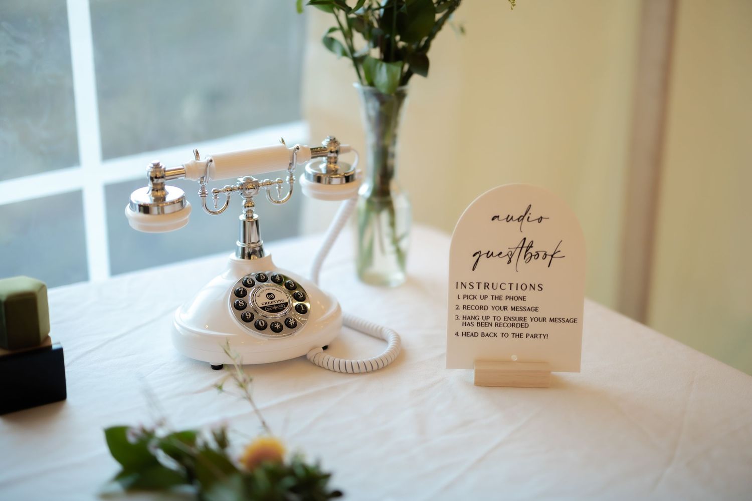 White vintage rotary phone beside an audio guestbook sign on a white tablecloth at a wedding reception.