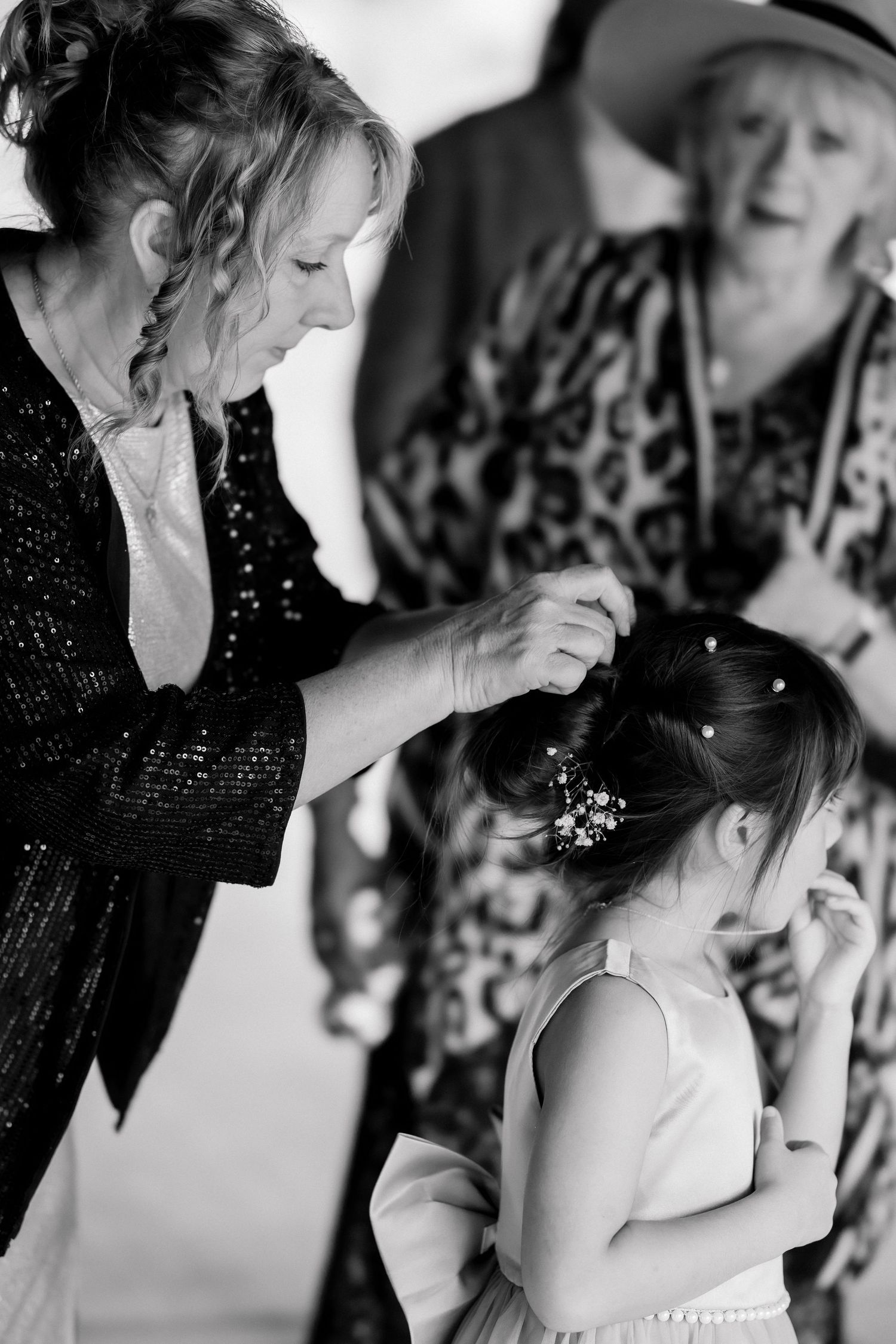 Woman arranging floral hair accessories in young girls updo hairstyle in black and white wedding photo.