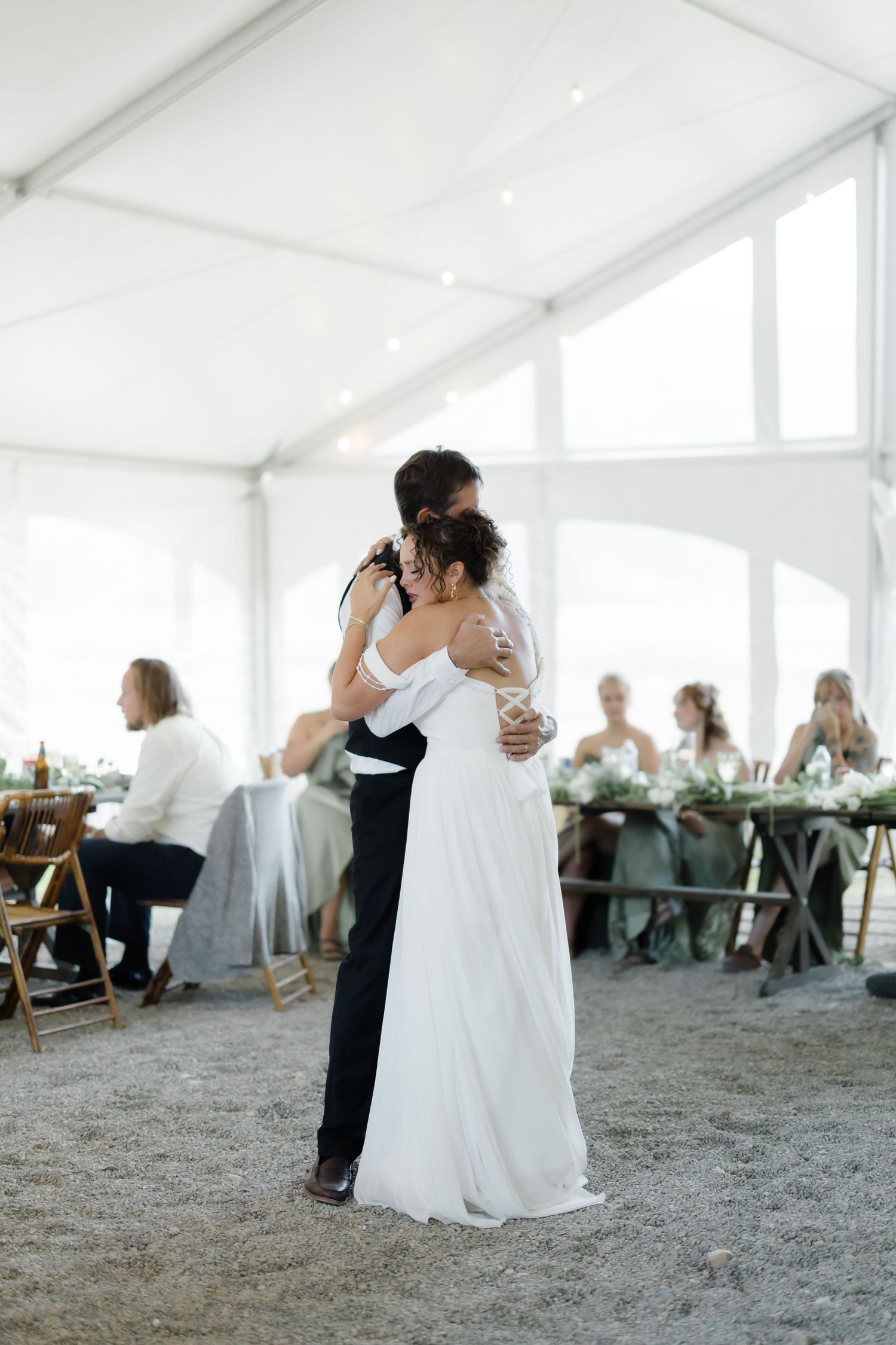 A bride and groom share a romantic first dance embrace inside a bright white wedding tent.