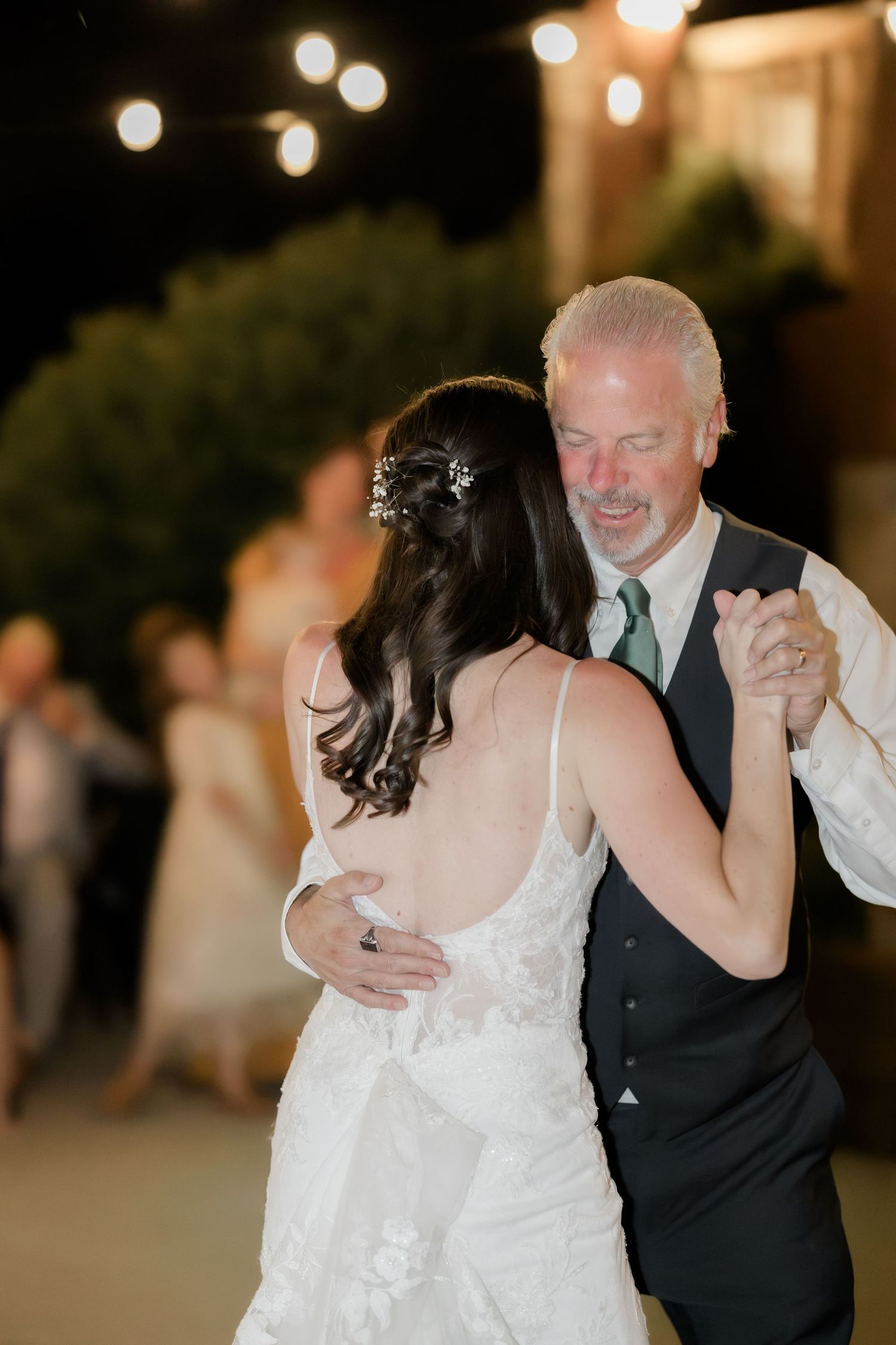 Bride and older man share an emotional father-daughter dance at an outdoor evening wedding reception.