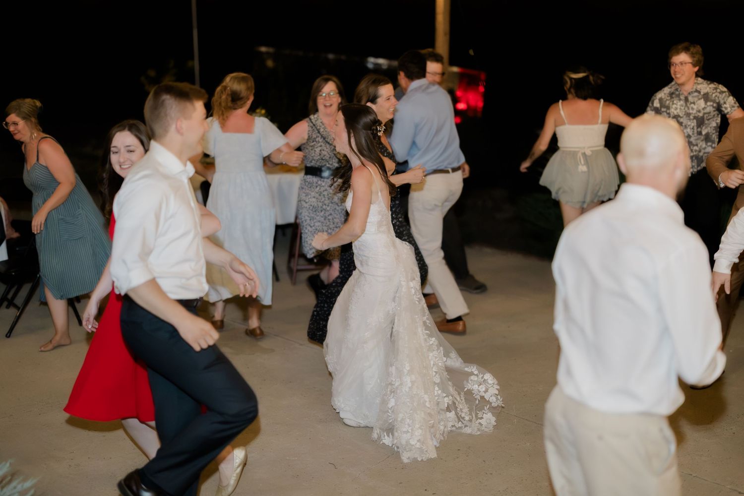 Bride and groom dancing with guests at an outdoor wedding reception at night.
