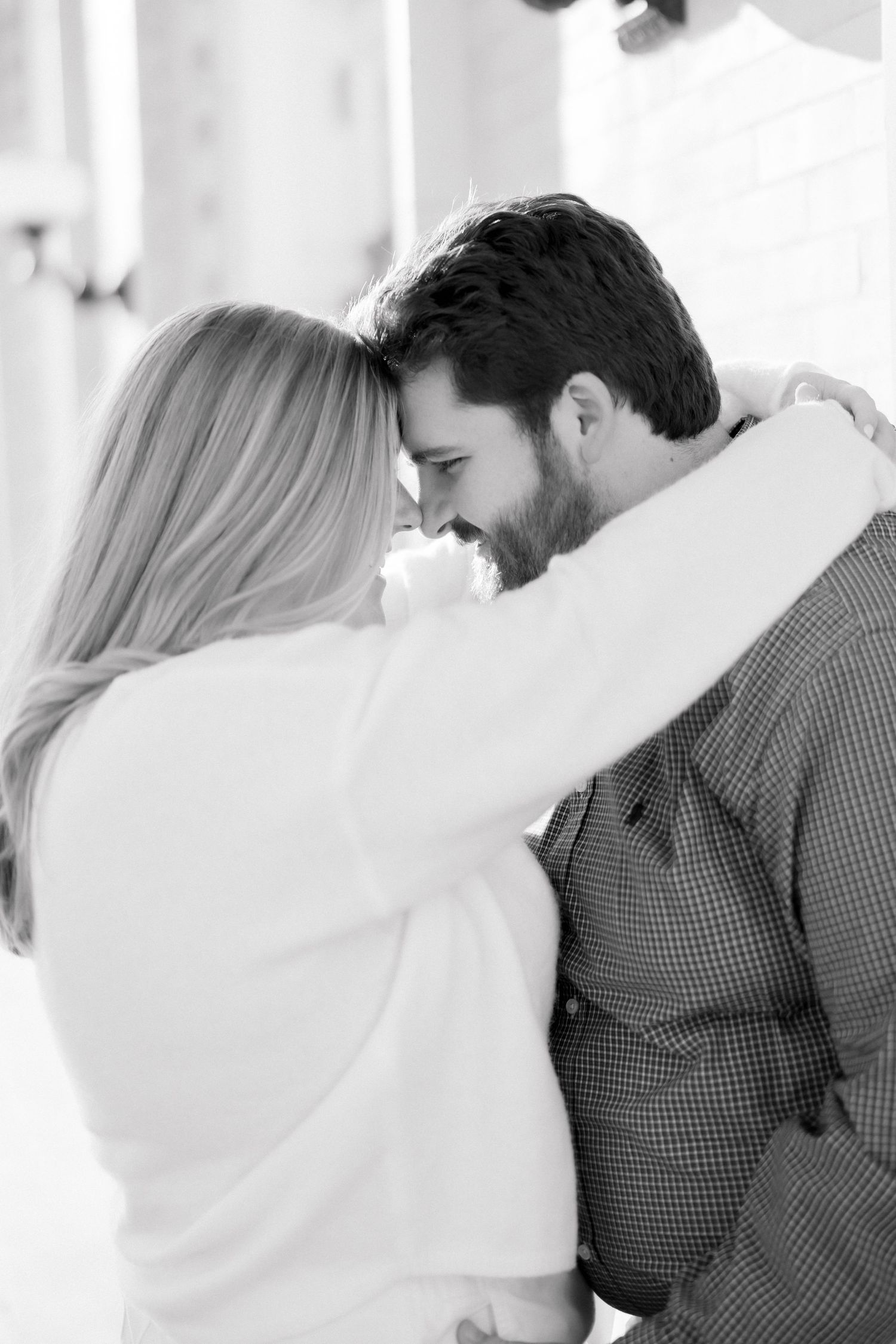 Black and white photo of a couple embracing closely, smiling and touching foreheads in a romantic moment.