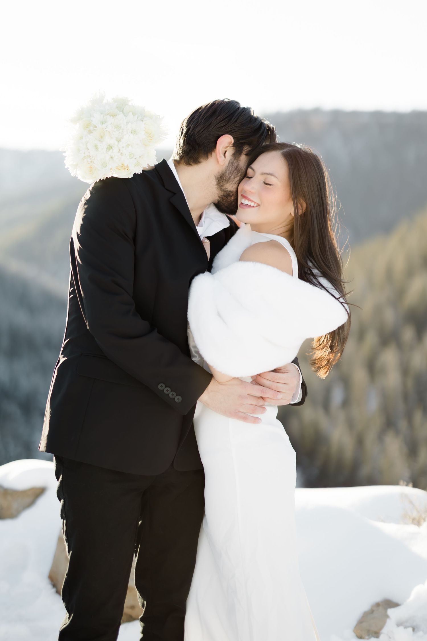 Romantic winter wedding embrace against a mountain backdrop with snow covered scenery. Pagosa Springs, Colorado. Piedra River Canyon.