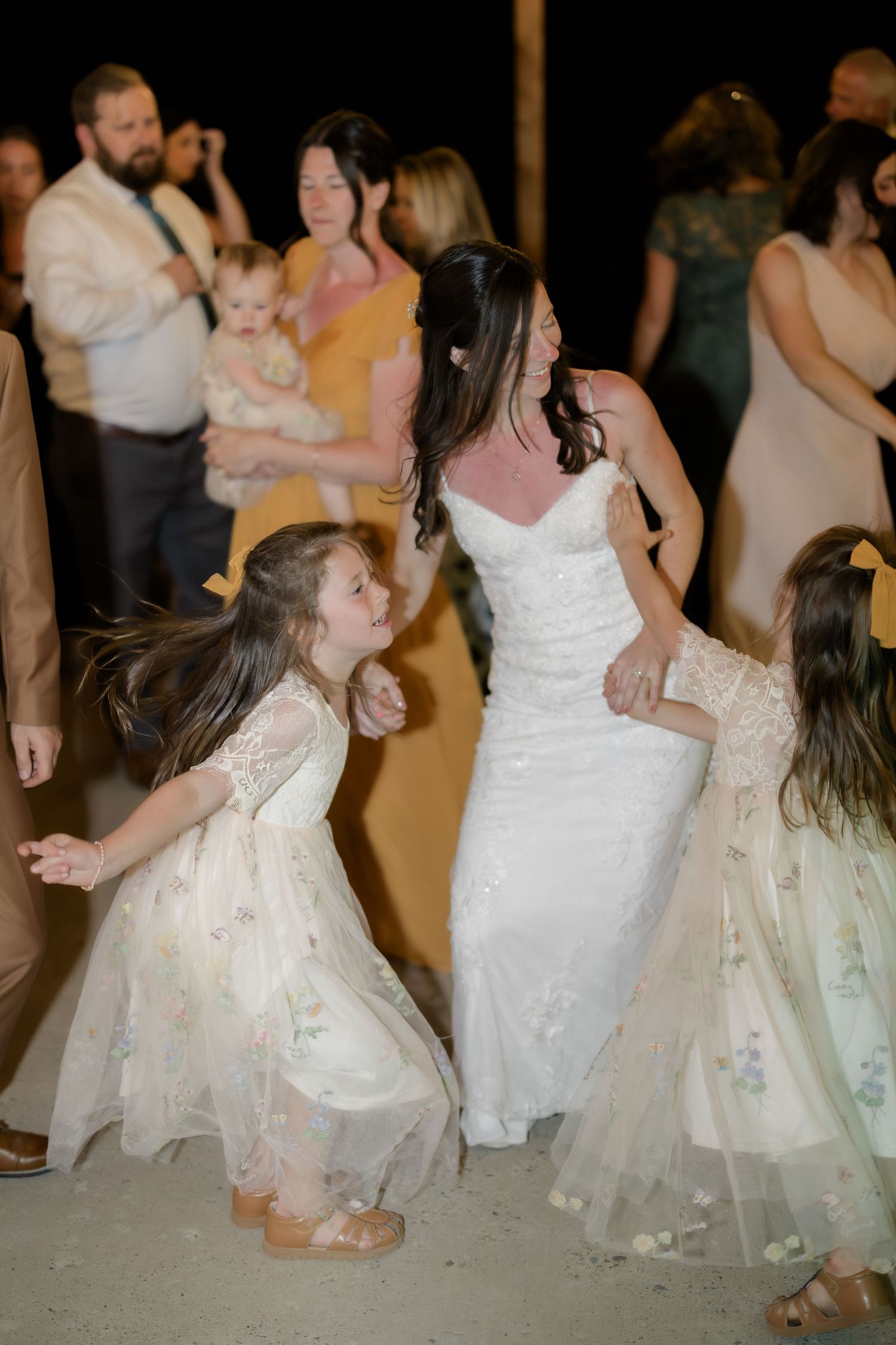 Bride dancing joyfully with two flower girls in white dresses at a wedding reception.