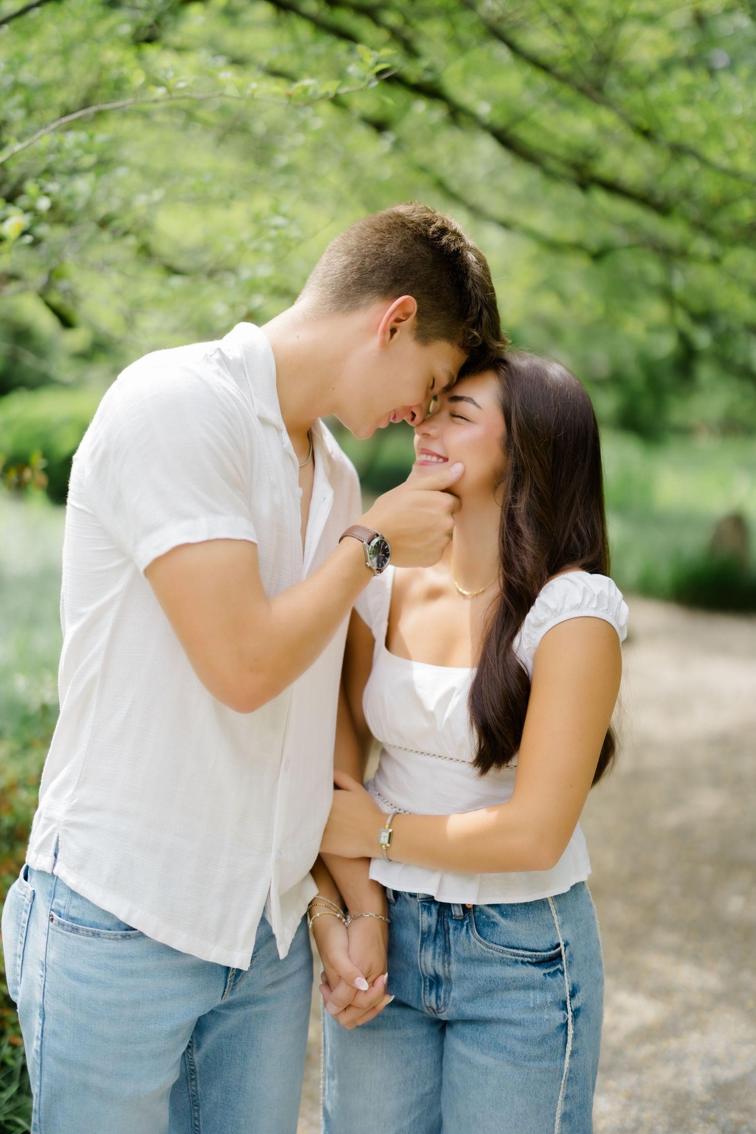 Young couple sharing a romantic moment in a lush green park, holding hands and smiling at each other.