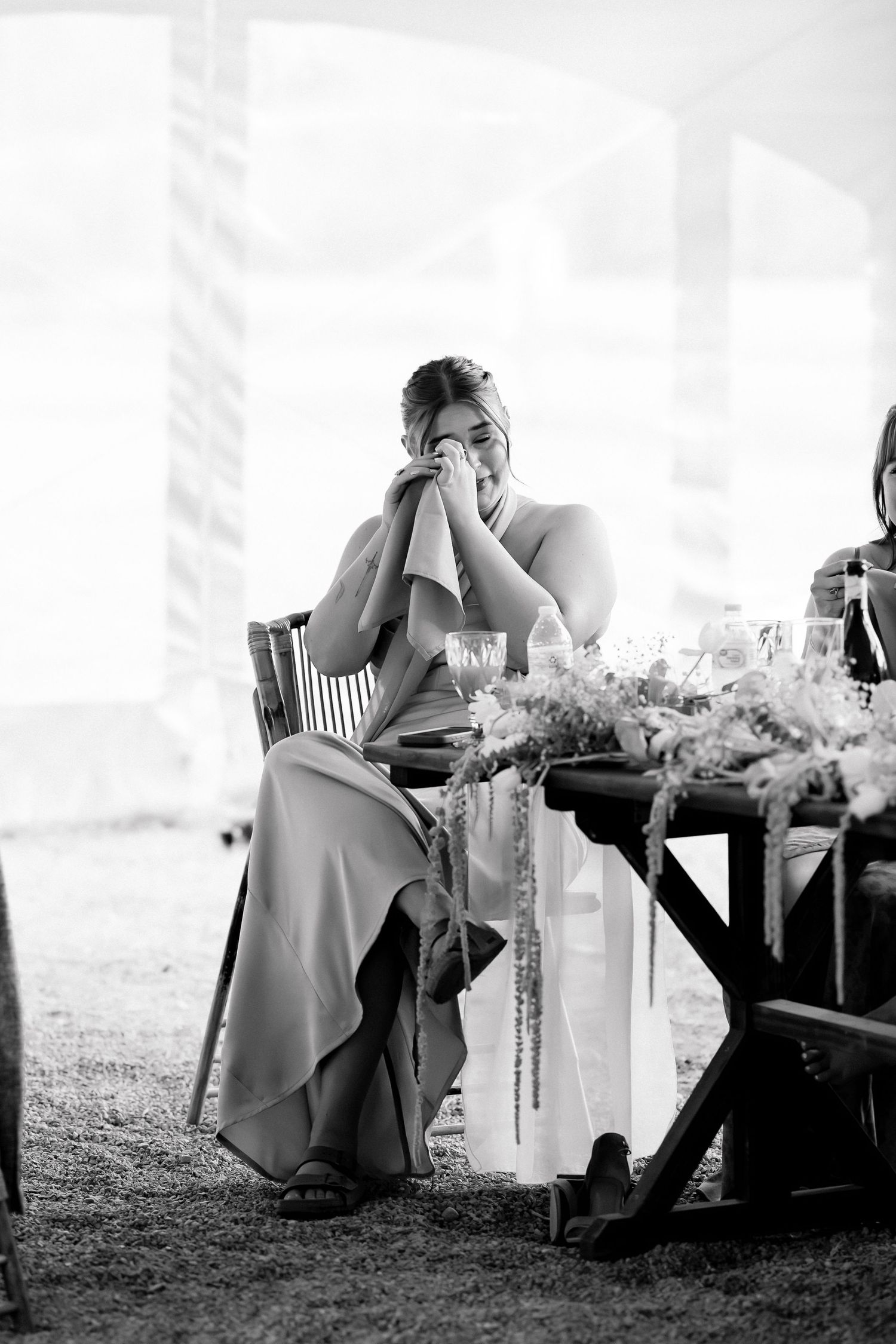 Black and white photo of emotional bridesmaid covering face with hands at wedding reception table.