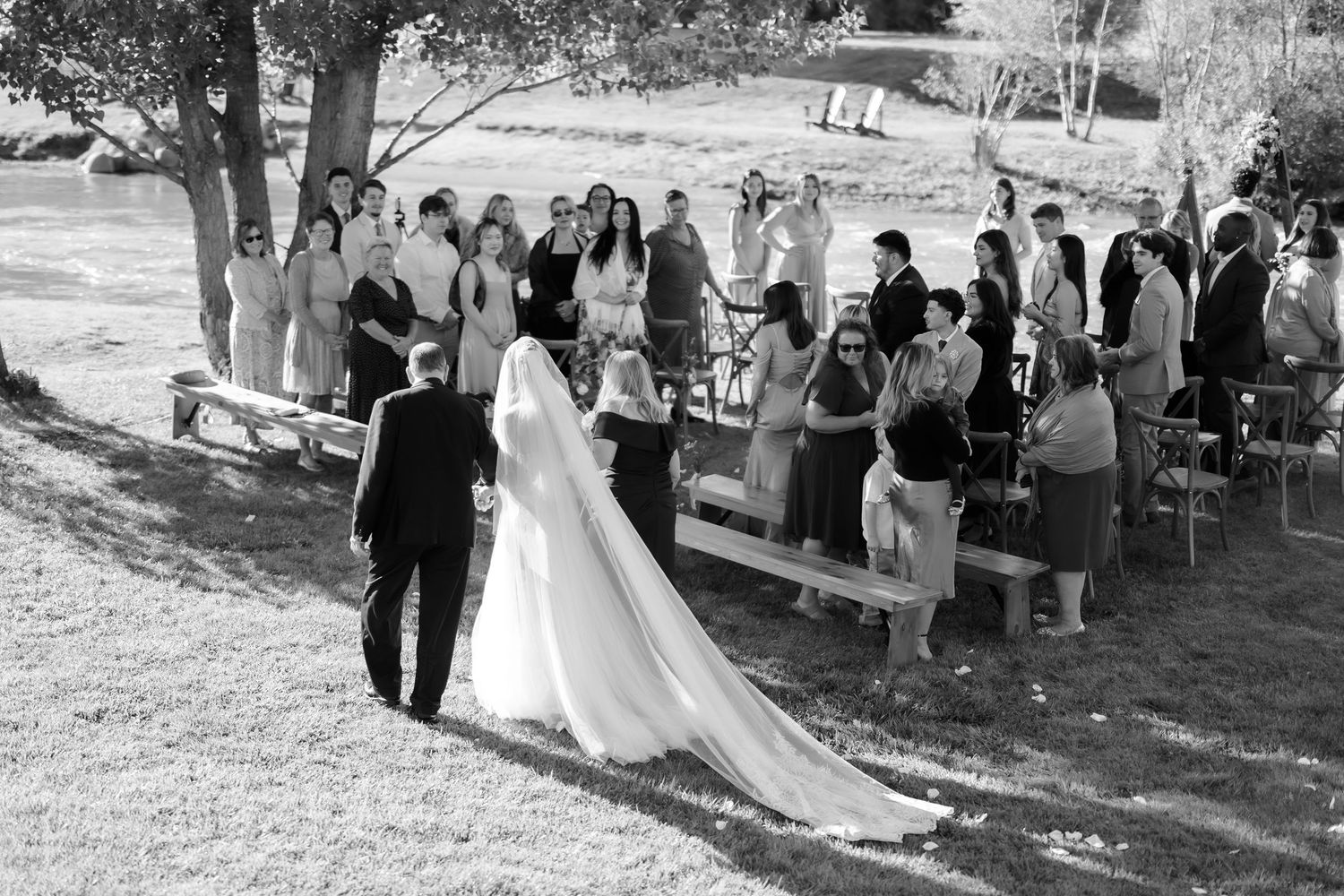 Black and white photo of a bride walking down the aisle outdoors with guests standing on either side.