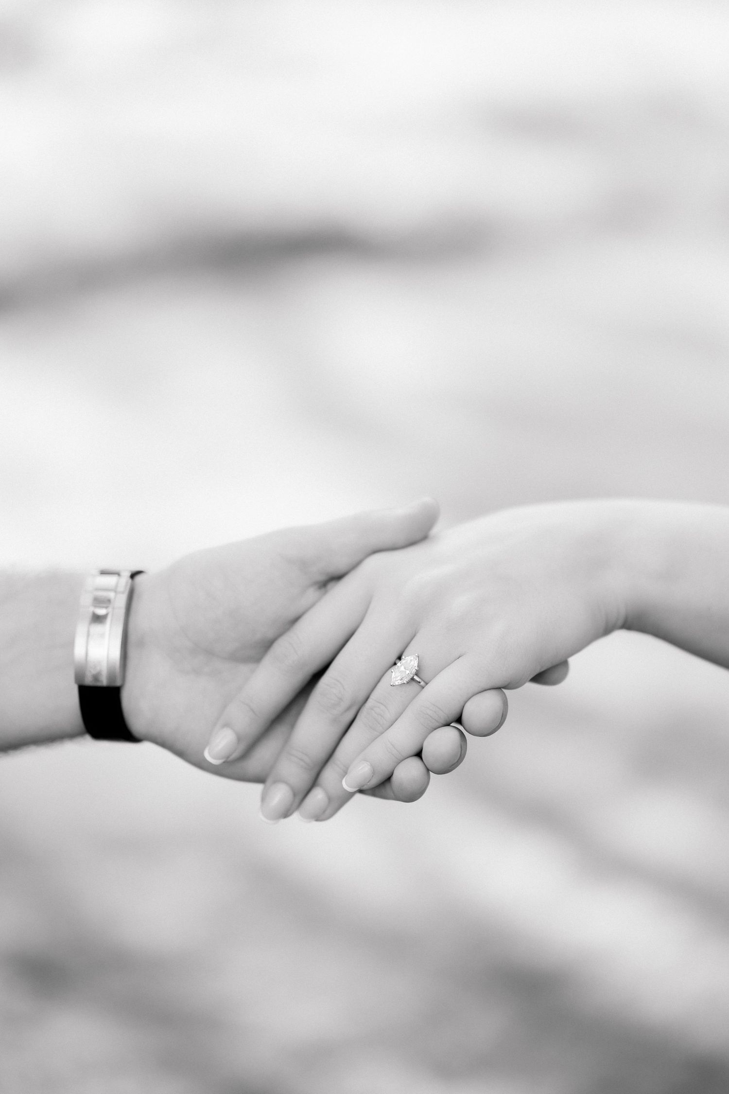 Black and white photo of couple holding hands, woman with diamond engagement ring, man wearing silver bracelet.
