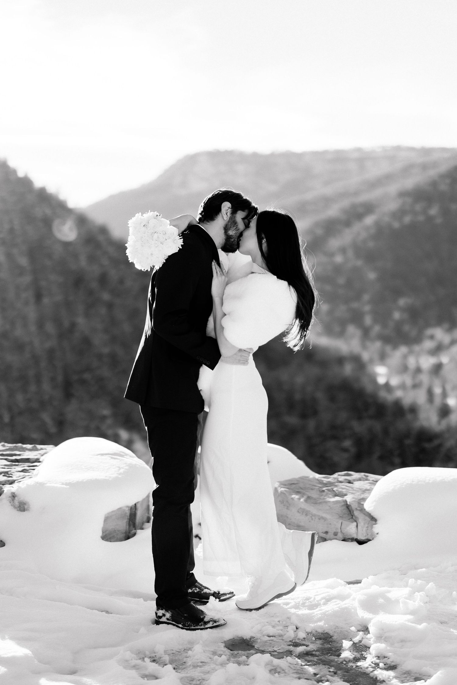 Black and white photo of bride and groom sharing a kiss in a snowy mountain landscape.