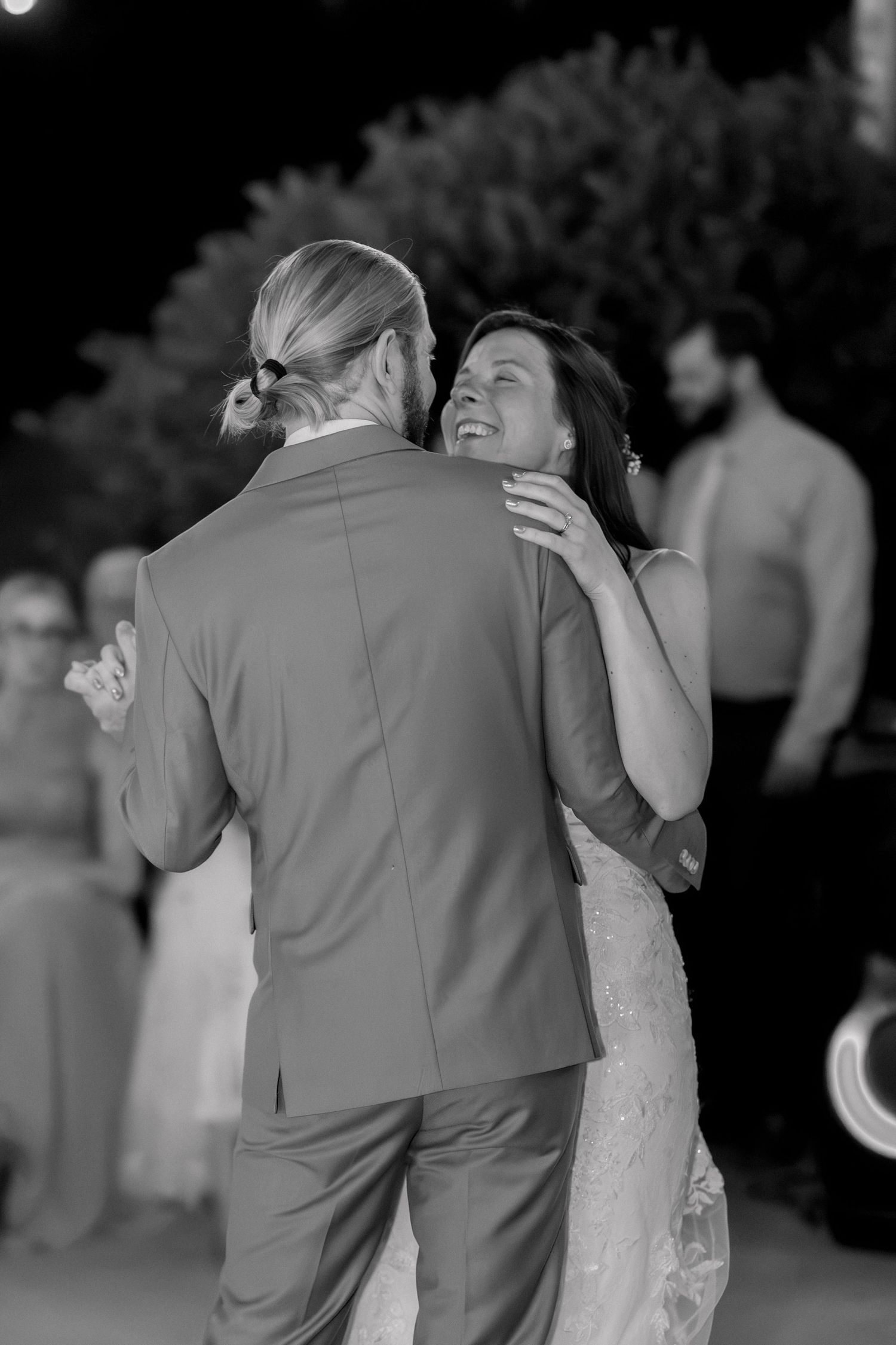 Black and white photo of a bride and groom sharing their first dance, smiling joyfully at an outdoor wedding reception.