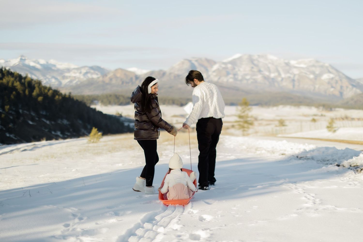 A winter engagement photoshoot featuring a couple in the snow with mountain views.