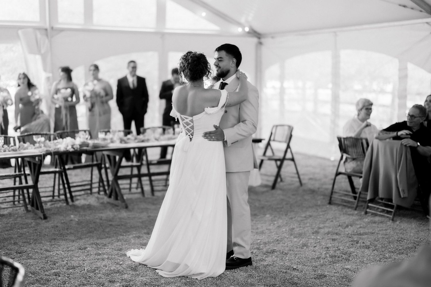 Bride and groom share their first dance under a white tent at an elegant outdoor wedding reception.