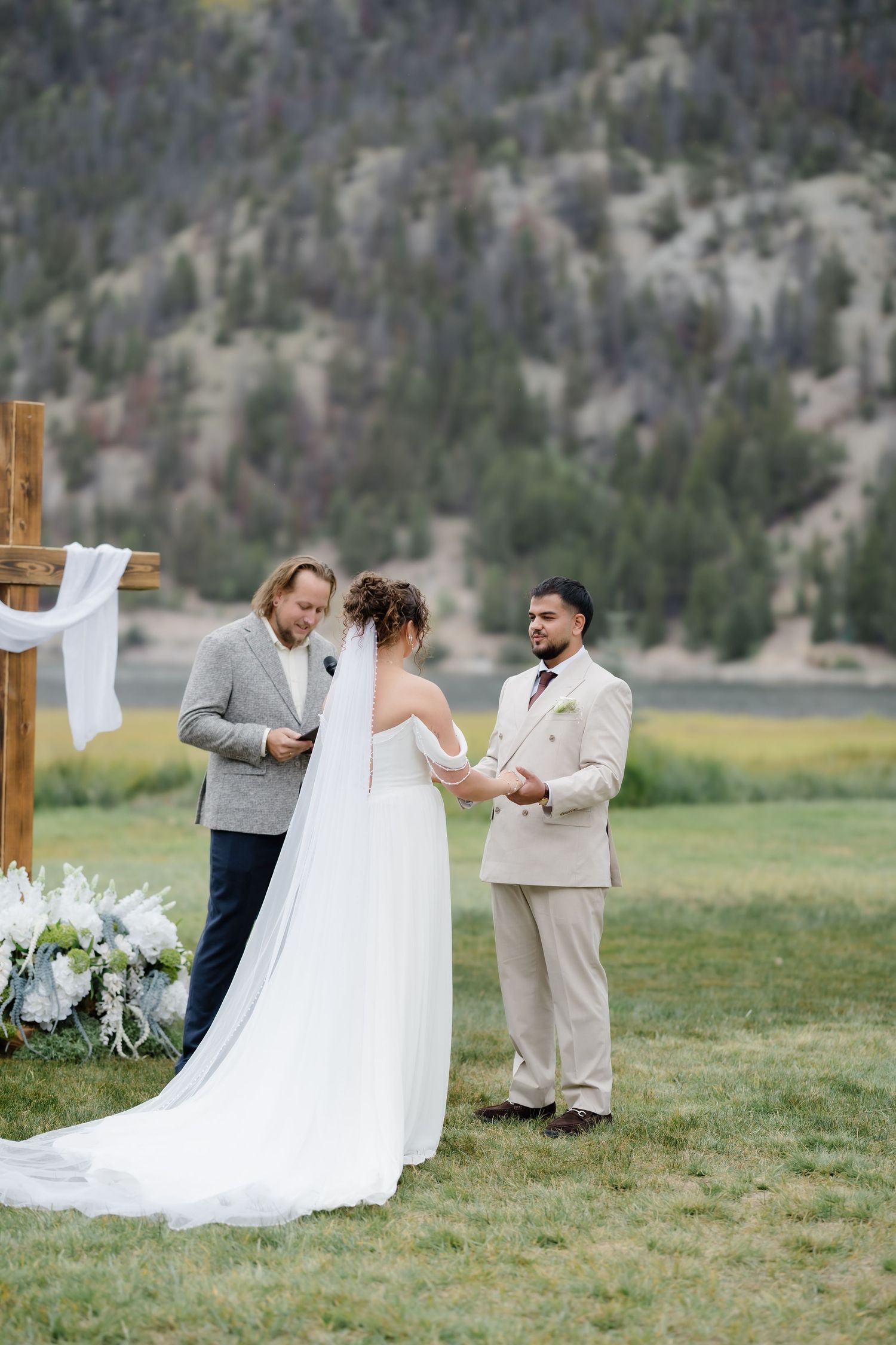 Outdoor wedding ceremony with bride and groom exchanging vows before an officiant, set against a scenic mountain backdrop.