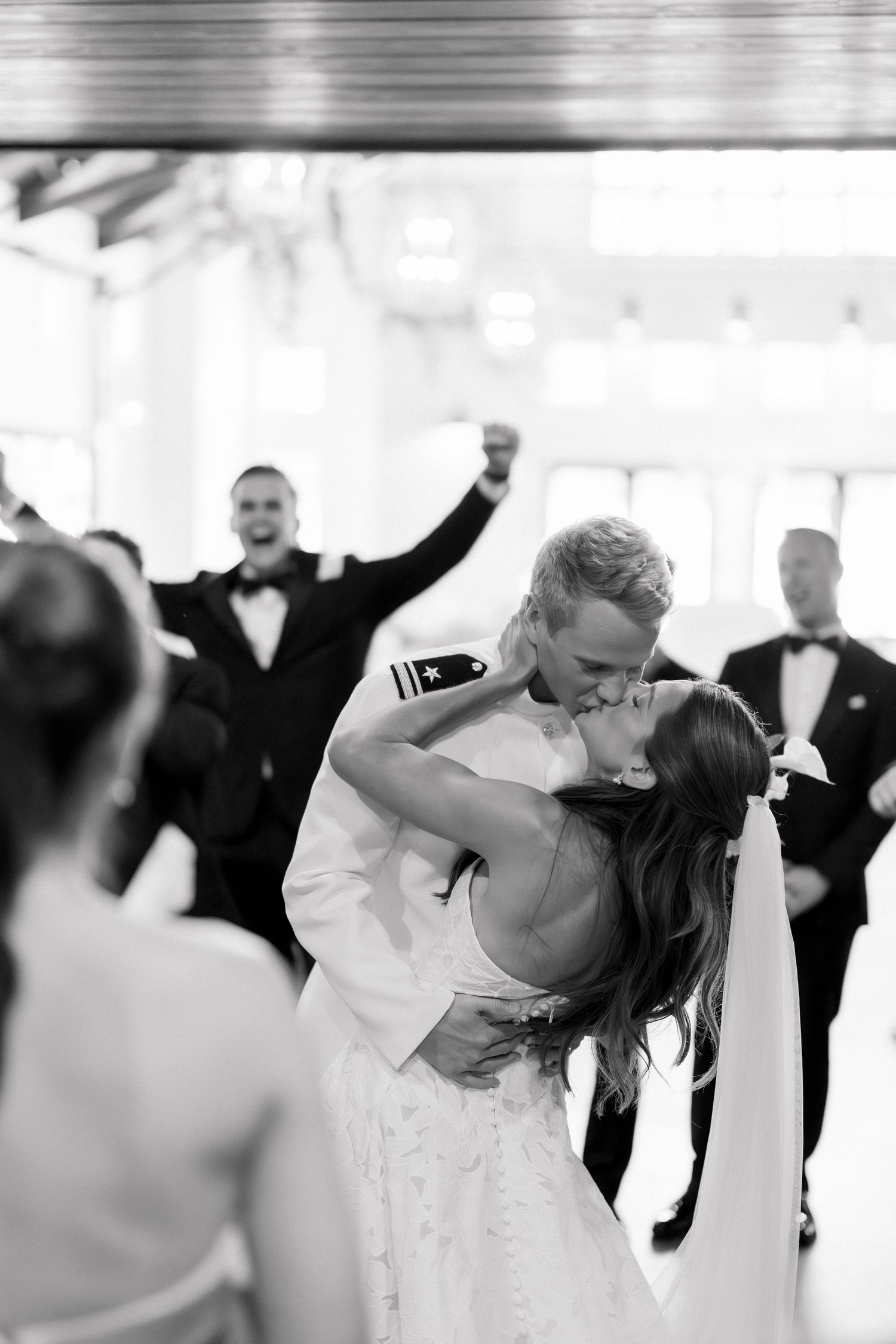 Black and white photo of a military groom dipping and kissing his bride on the dance floor at their wedding reception.