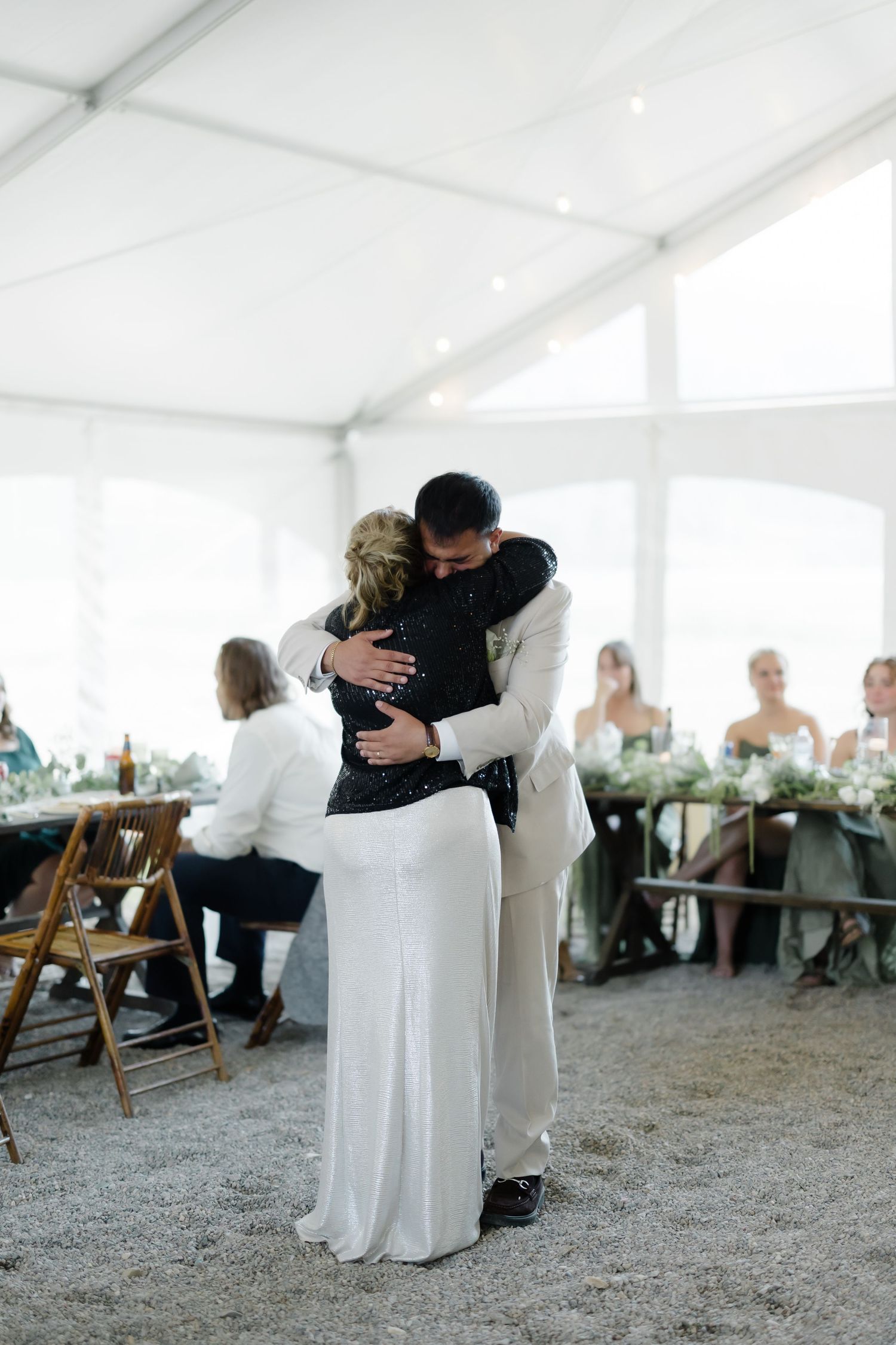 Newlyweds share a tender hug during their first dance at an elegant tented wedding reception.