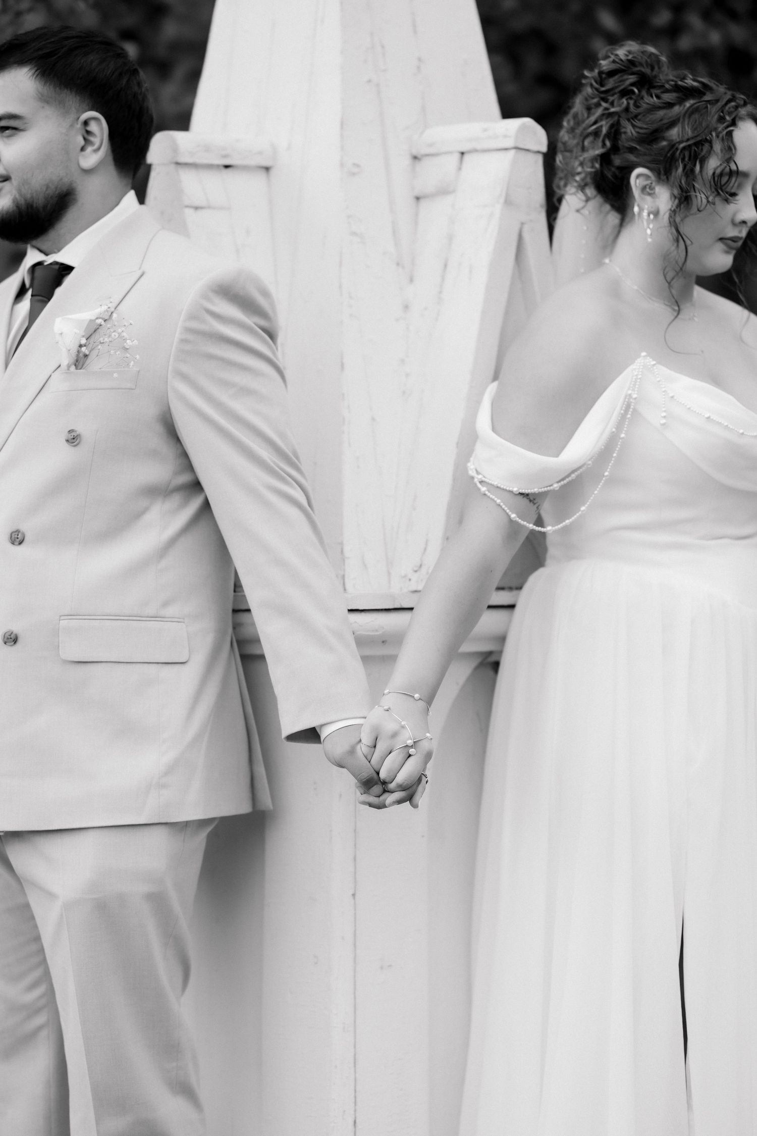 Black and white photo of a bride and groom holding hands behind their backs at their wedding ceremony.