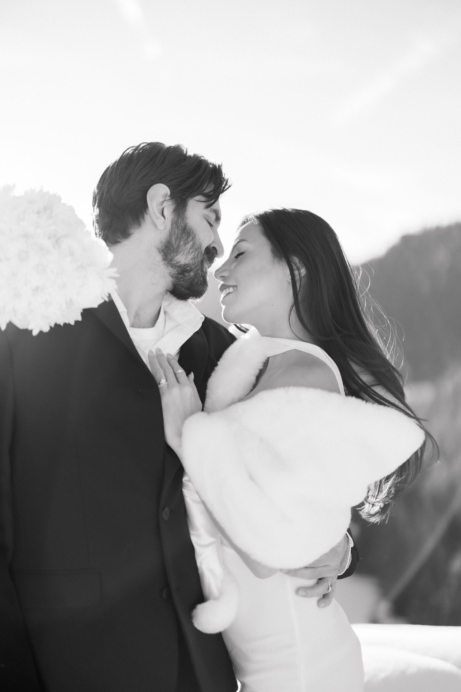 Black and white close-up of bride and groom about to kiss, bride in fur wrap holding bouquet.