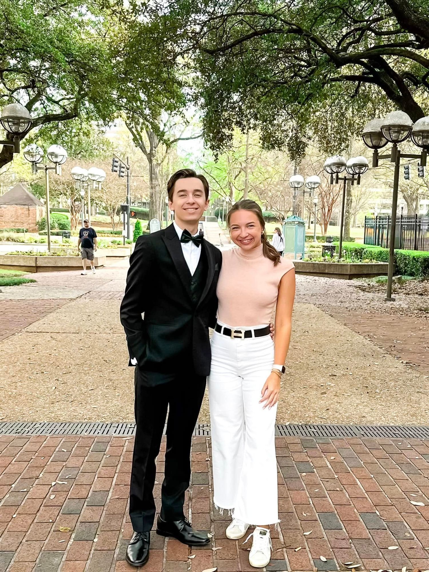 Two people in formal attire pose together on brick pavement under trees in Birmingham, Alabama.
